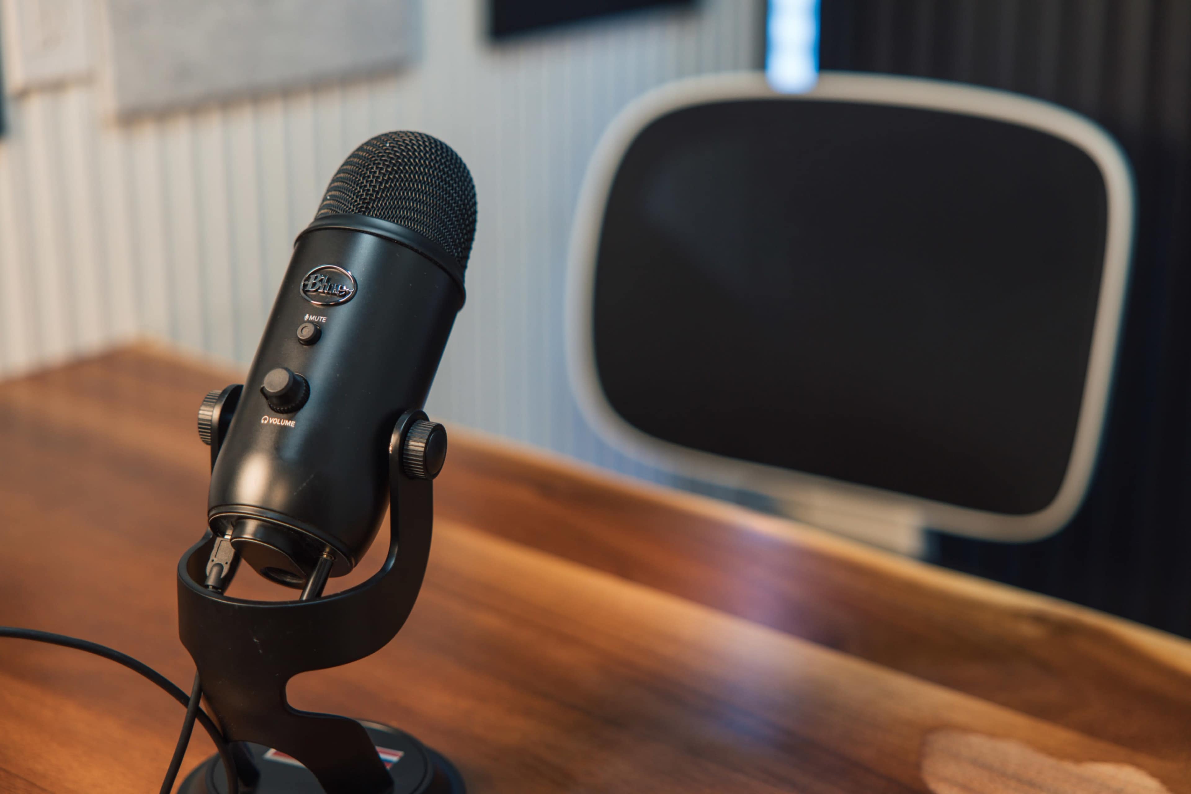 A black microphone is positioned on a wooden table next to an empty black chair.