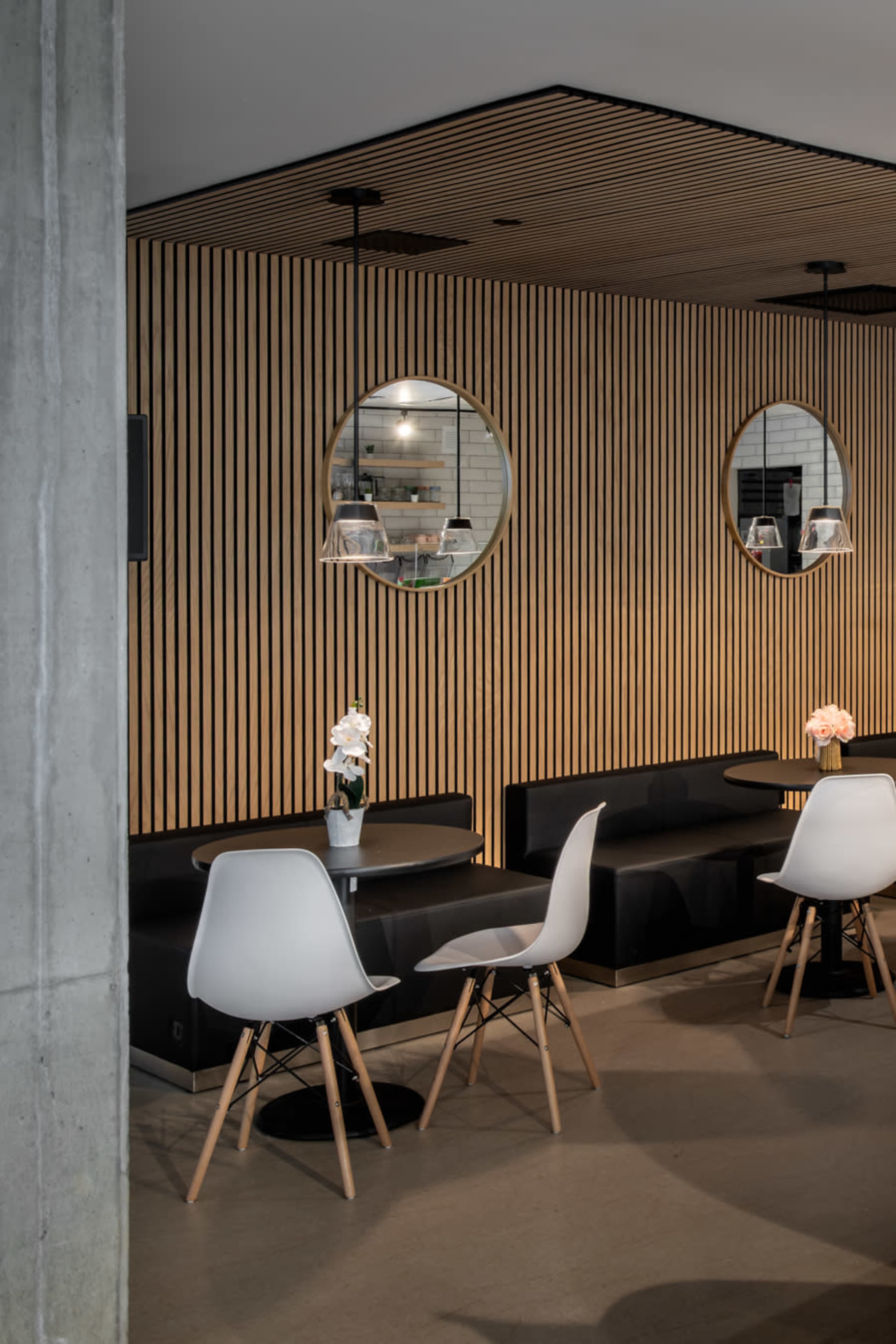 The image shows a modern café interior with round mirrors, wooden striped walls, black seating, and white chairs arranged around small tables.