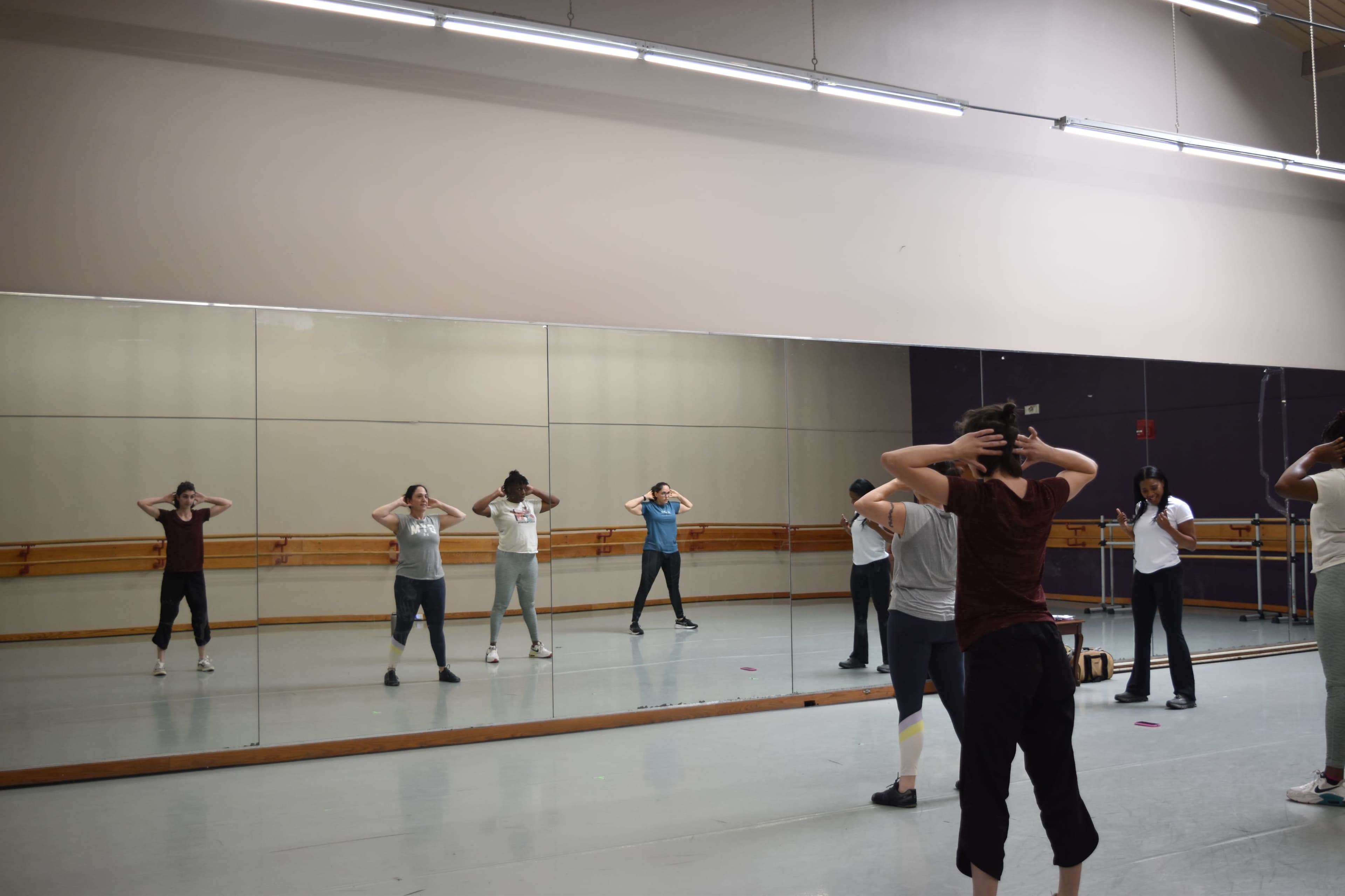 A group of people is practicing dance moves in a mirrored studio.