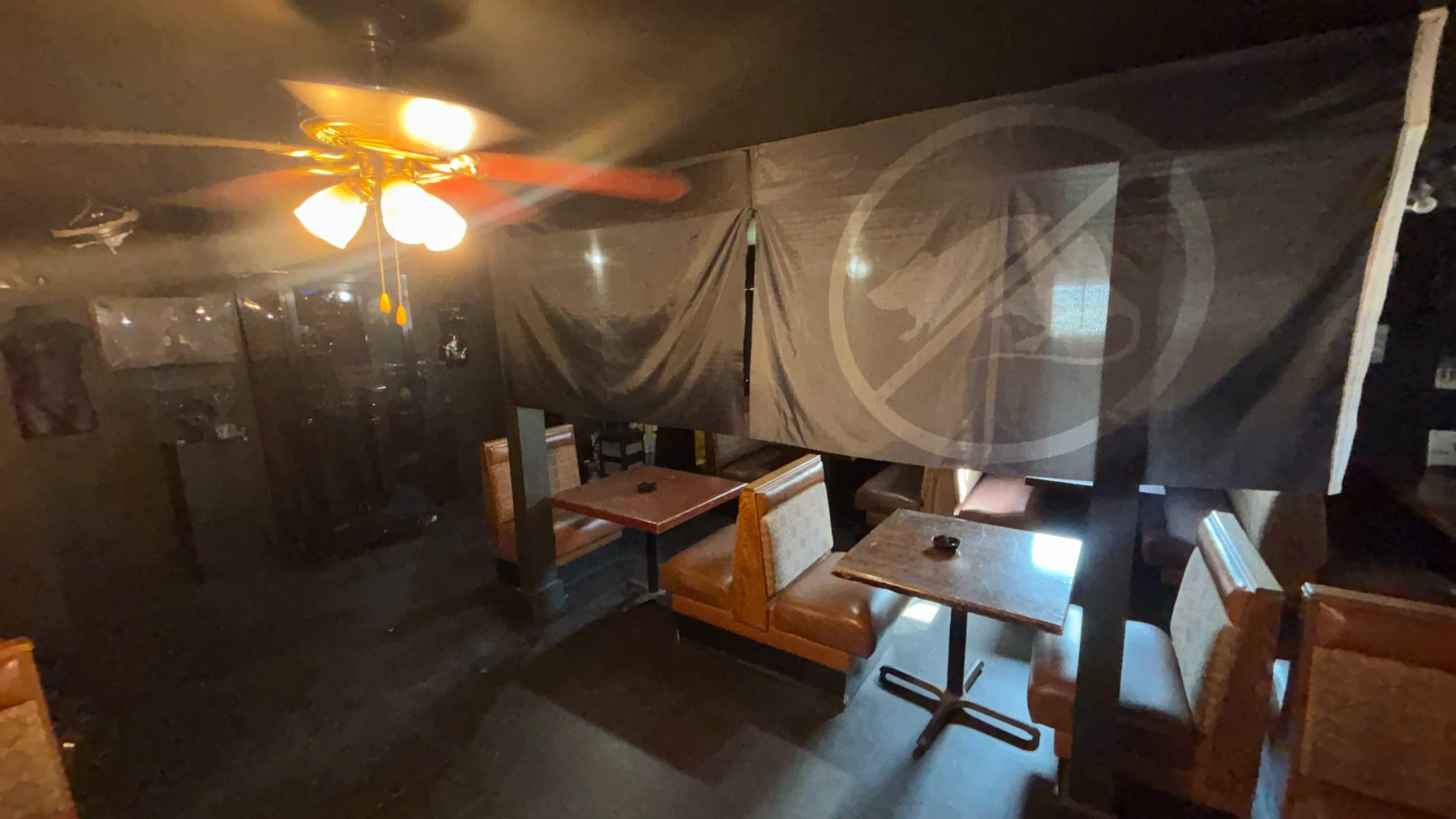 The image shows a dimly lit restaurant space featuring several booths and tables separated by dark curtains.