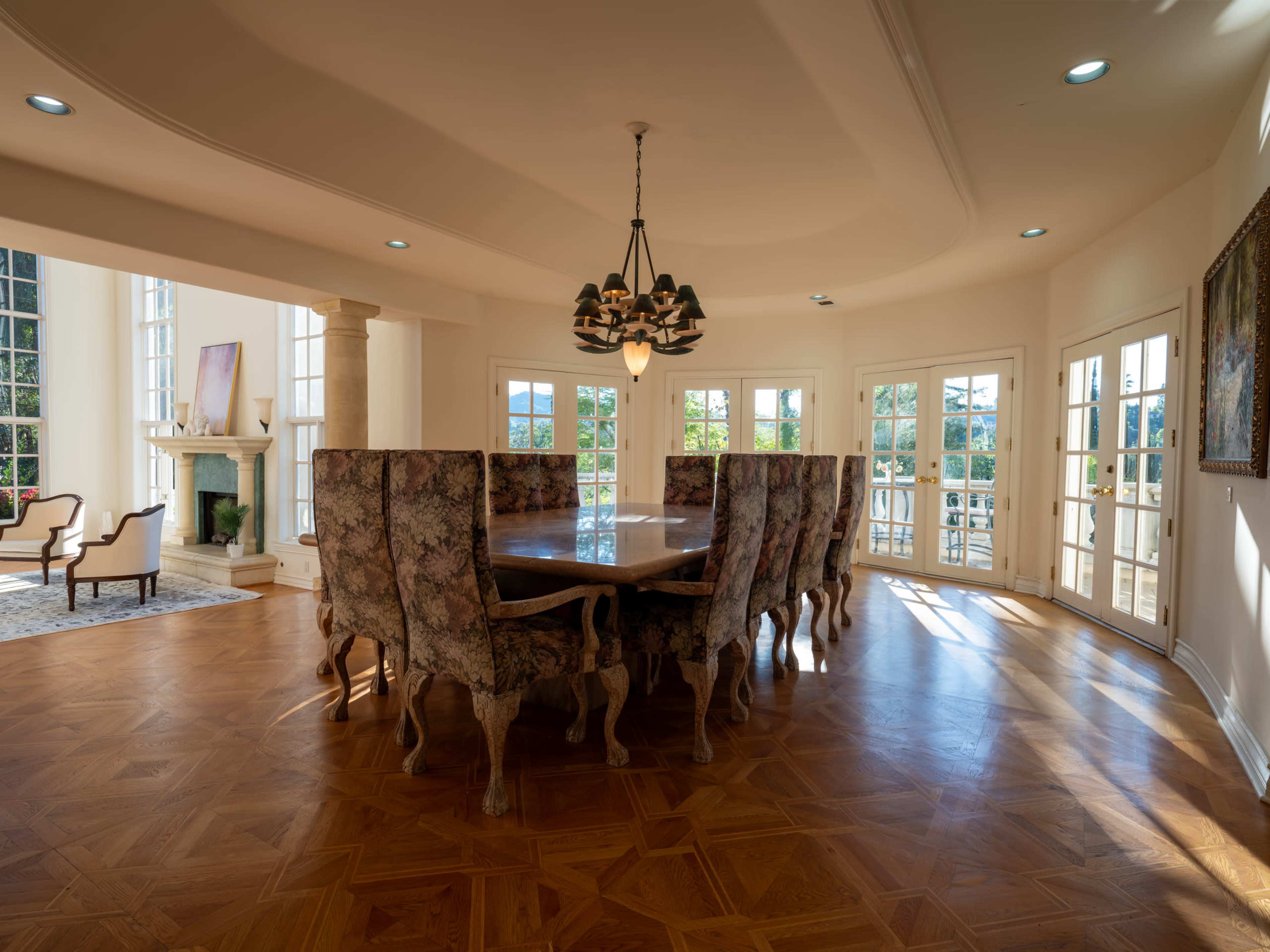 A spacious dining room features a large wooden table surrounded by upholstered chairs, with natural light streaming through multiple windows.