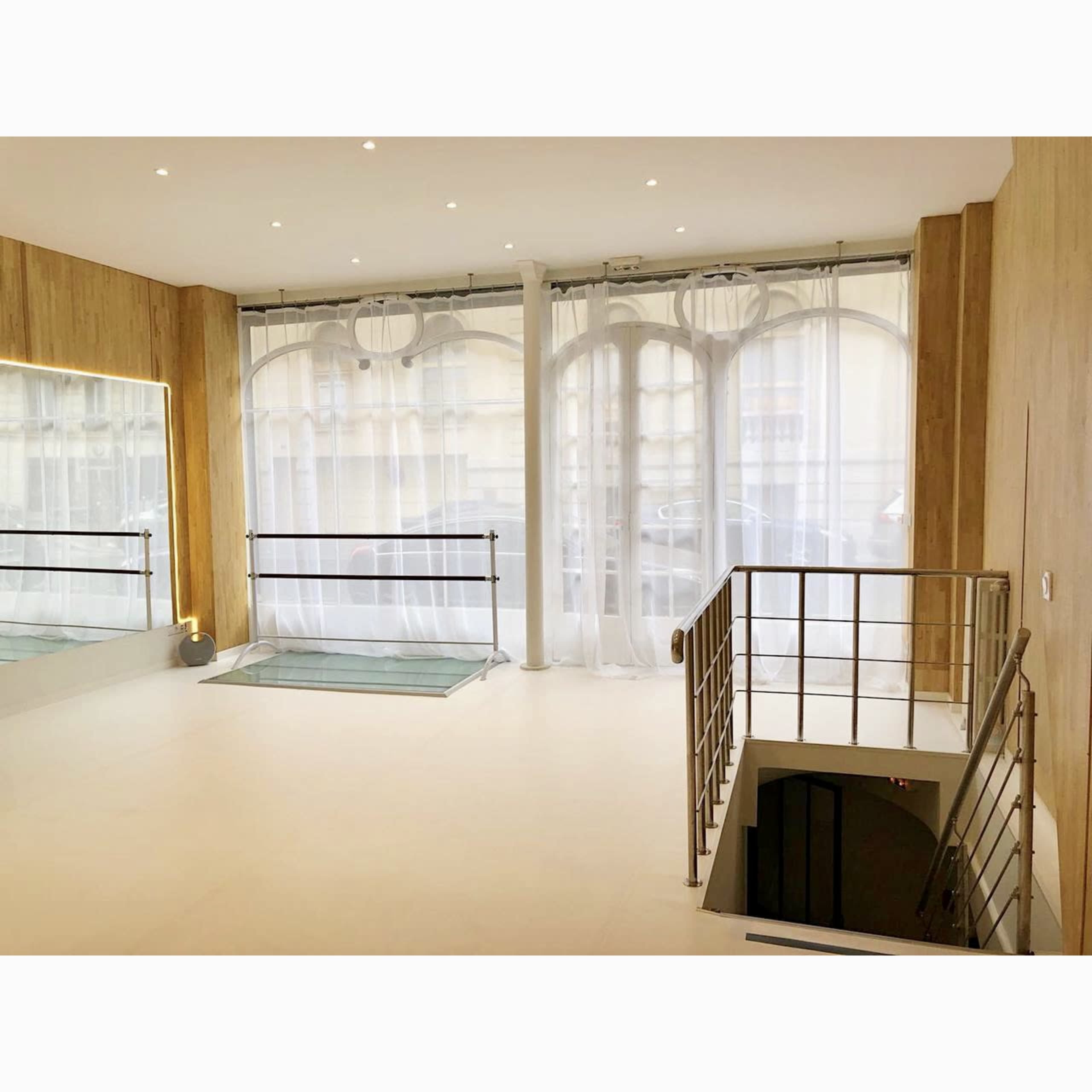 A spacious, modern room with large windows covered by sheer curtains and a staircase leading to a lower level.