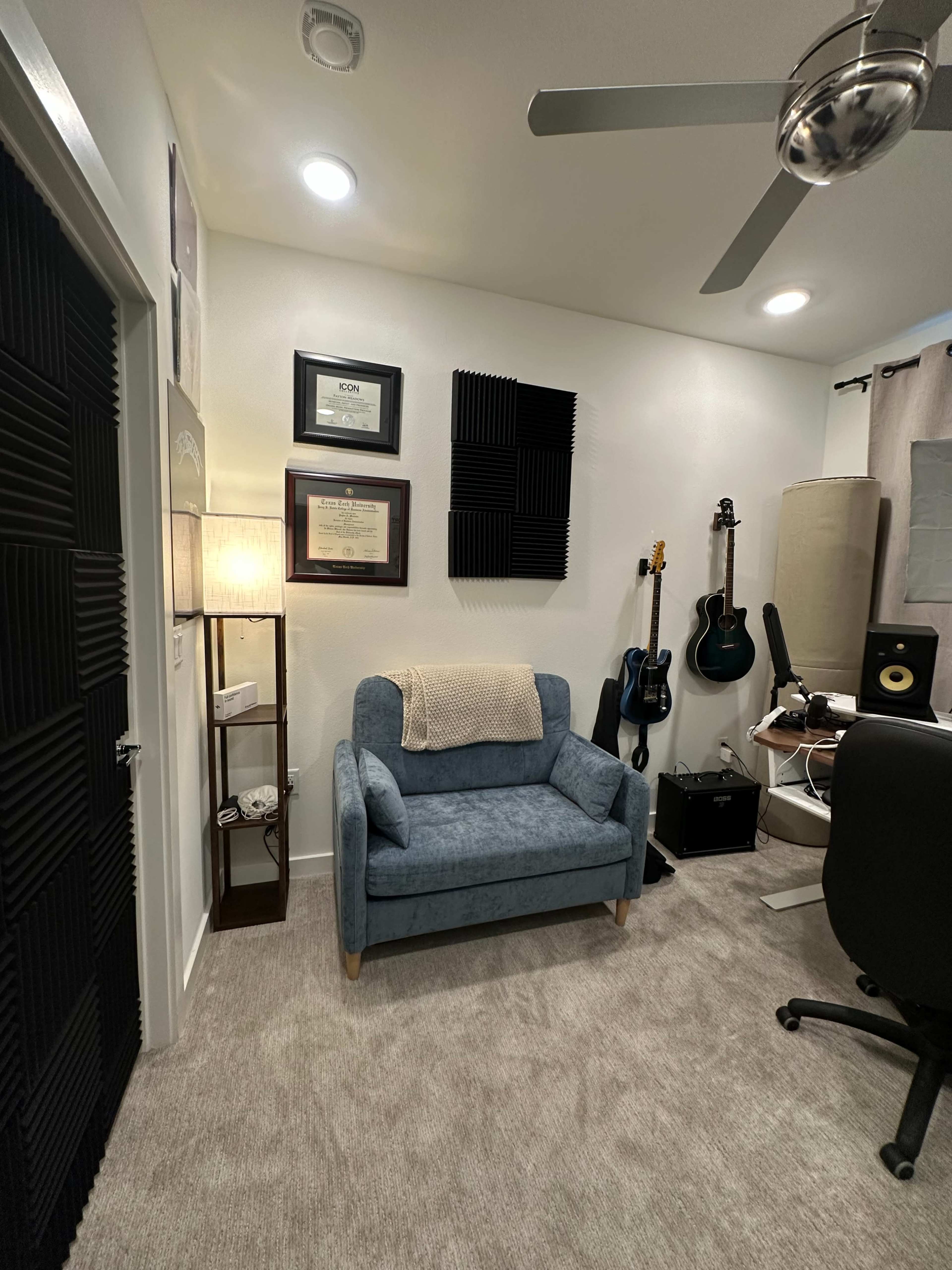 The image shows a room with a blue armchair, a lamp, musical instruments on the wall, and a desk with audio equipment.