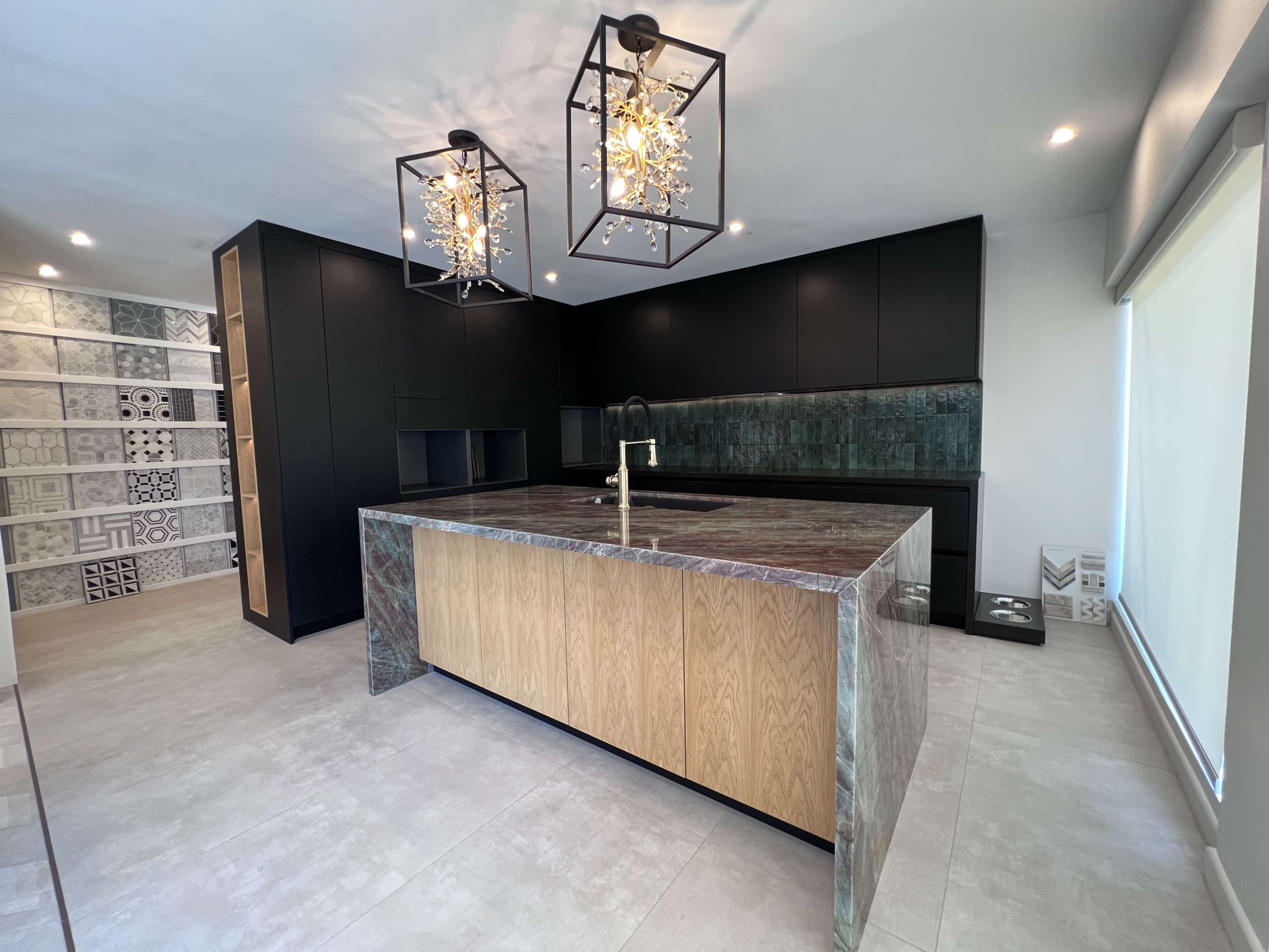 A modern kitchen featuring an island with an oak front and a green stone countertop, black cabinets, and decorative light fixtures.