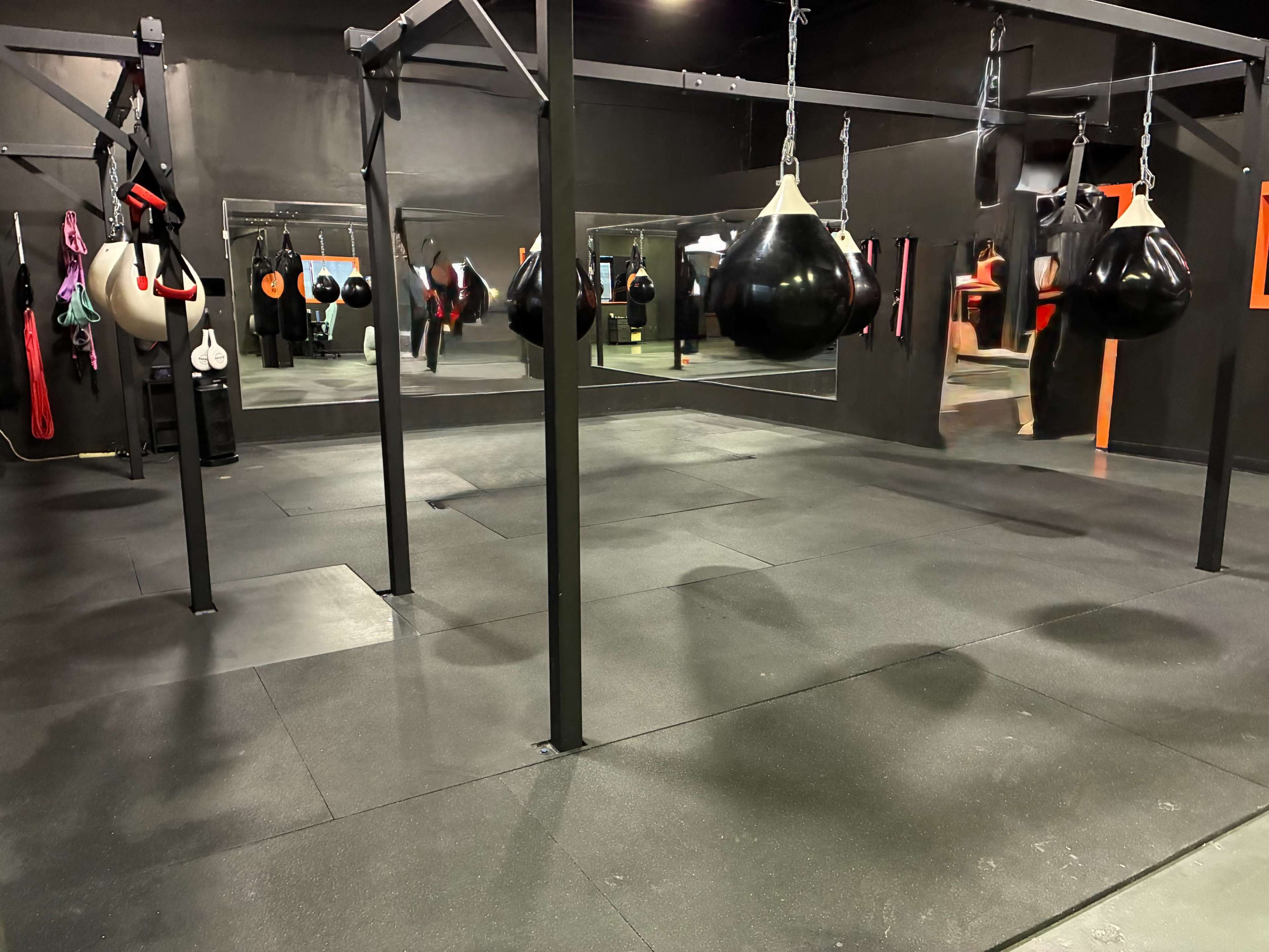 The image shows a boxing gym with hanging punching bags, mirrors, and various training equipment on the walls.