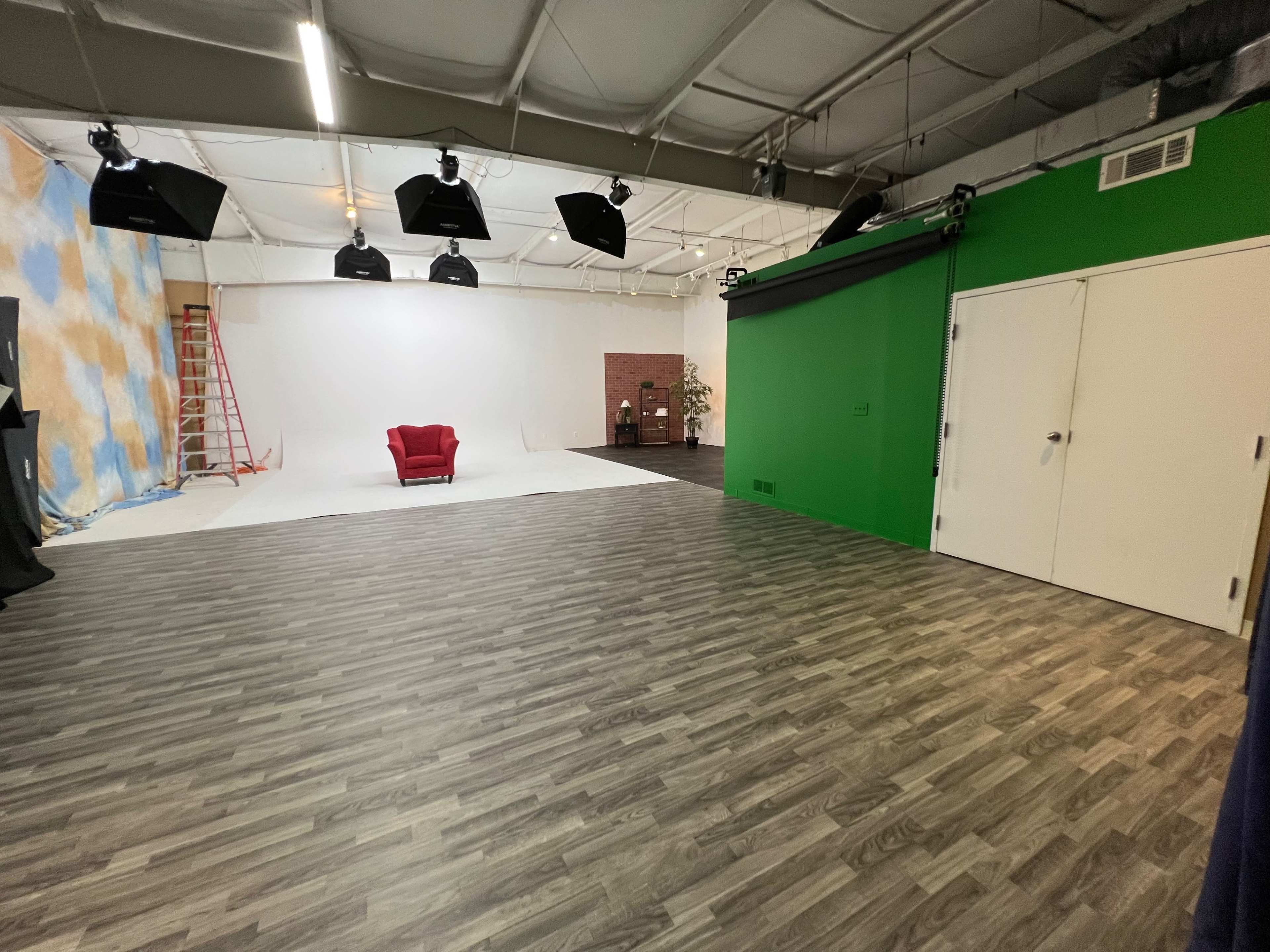 A photography studio with a red chair positioned on a white backdrop, surrounded by green and blue panels and a ladder in the background.