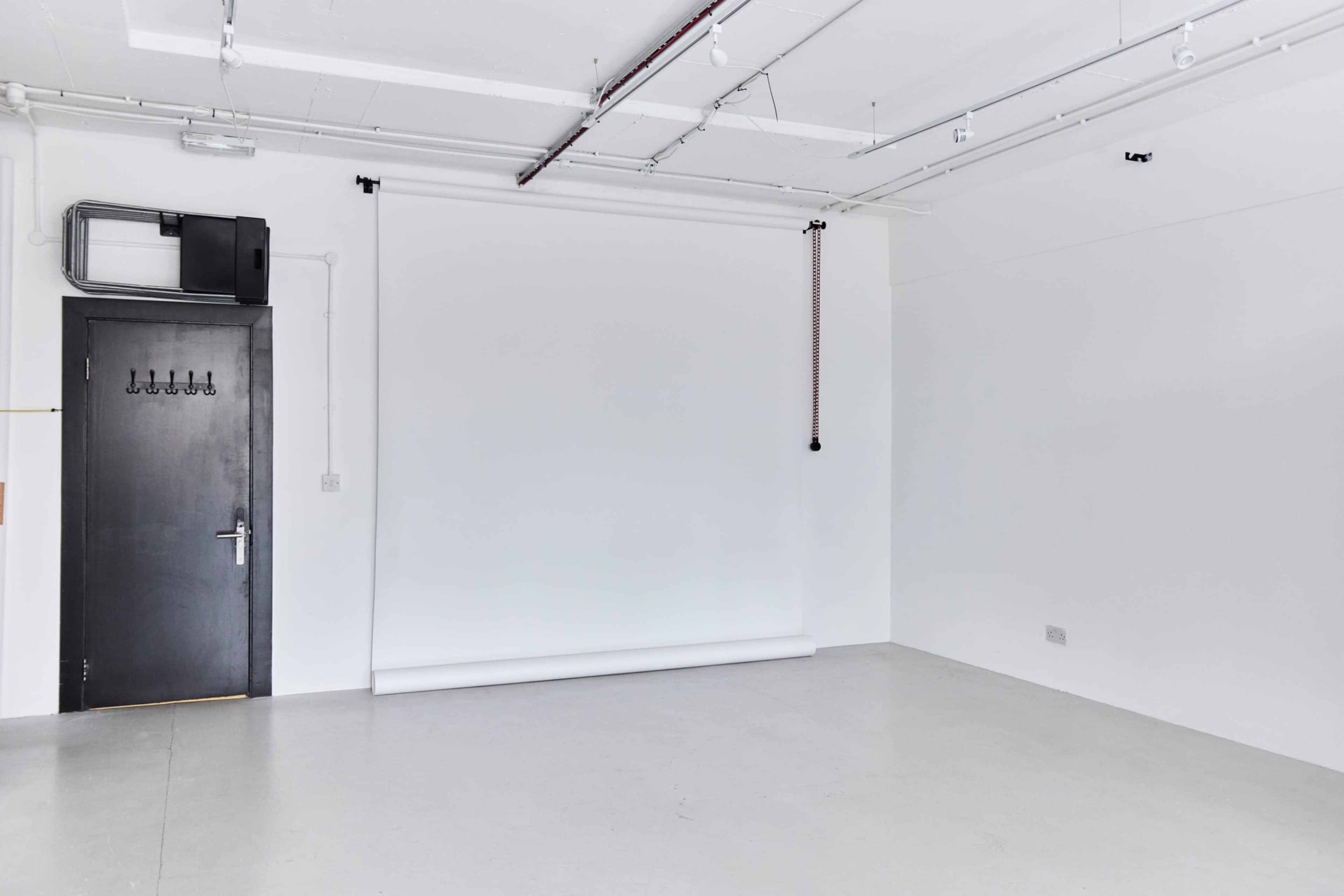 The image shows a minimalist studio space with a black door, a white backdrop, and plain white walls.