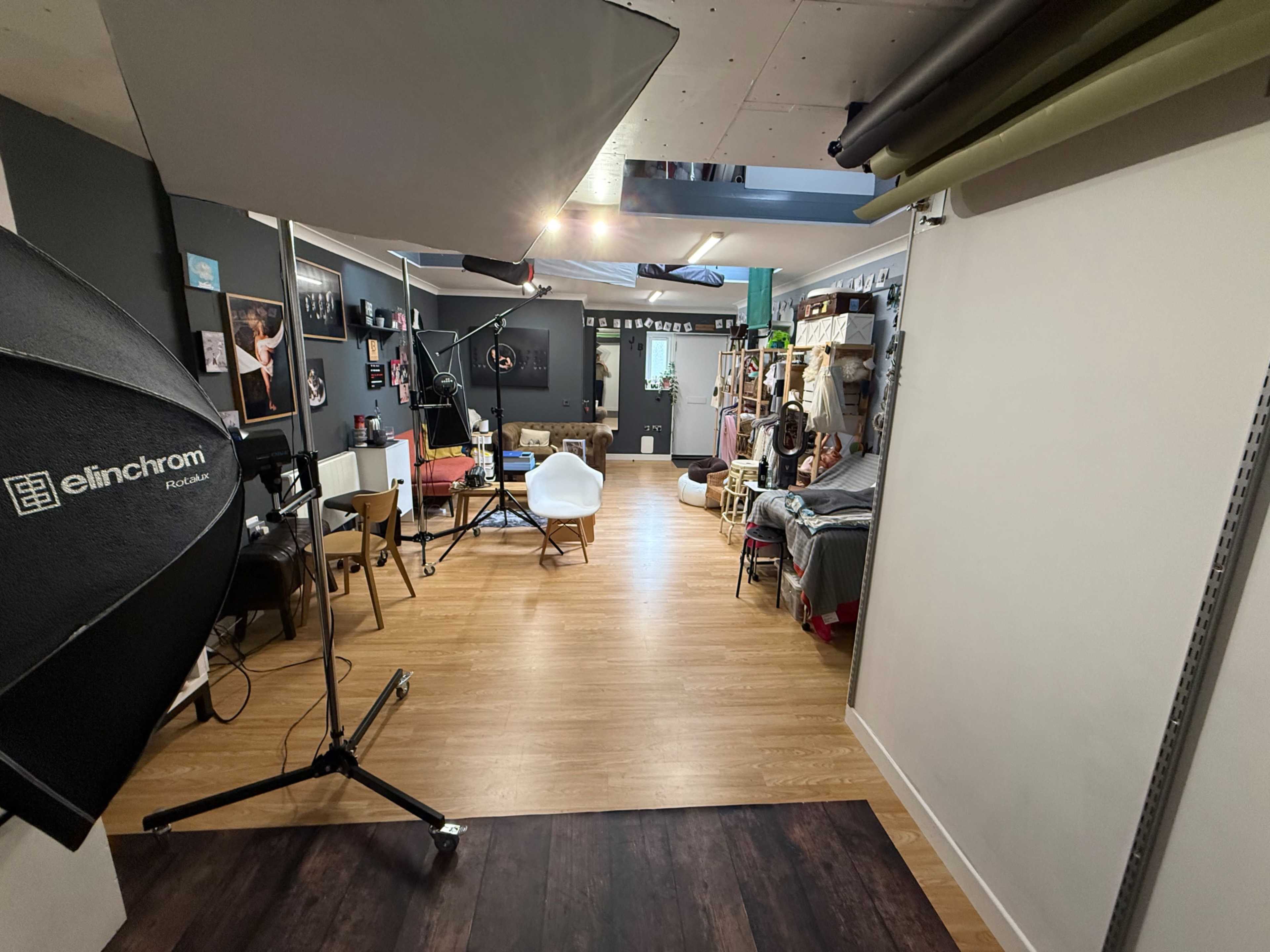 The image shows a well-lit photography studio featuring various props, lighting equipment, and a mix of furniture arranged in a spacious layout.