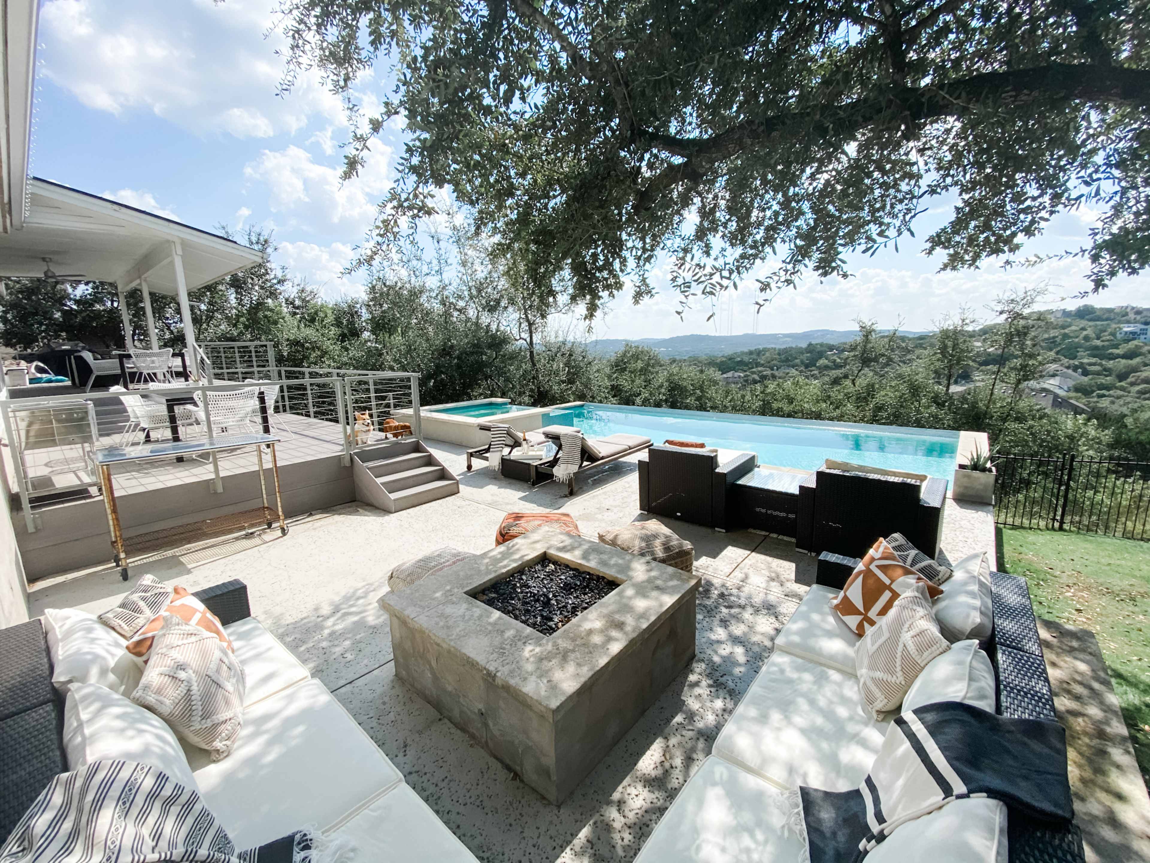 A backyard area with a pool, seating around a stone fire pit, and a scenic view of surrounding hills.