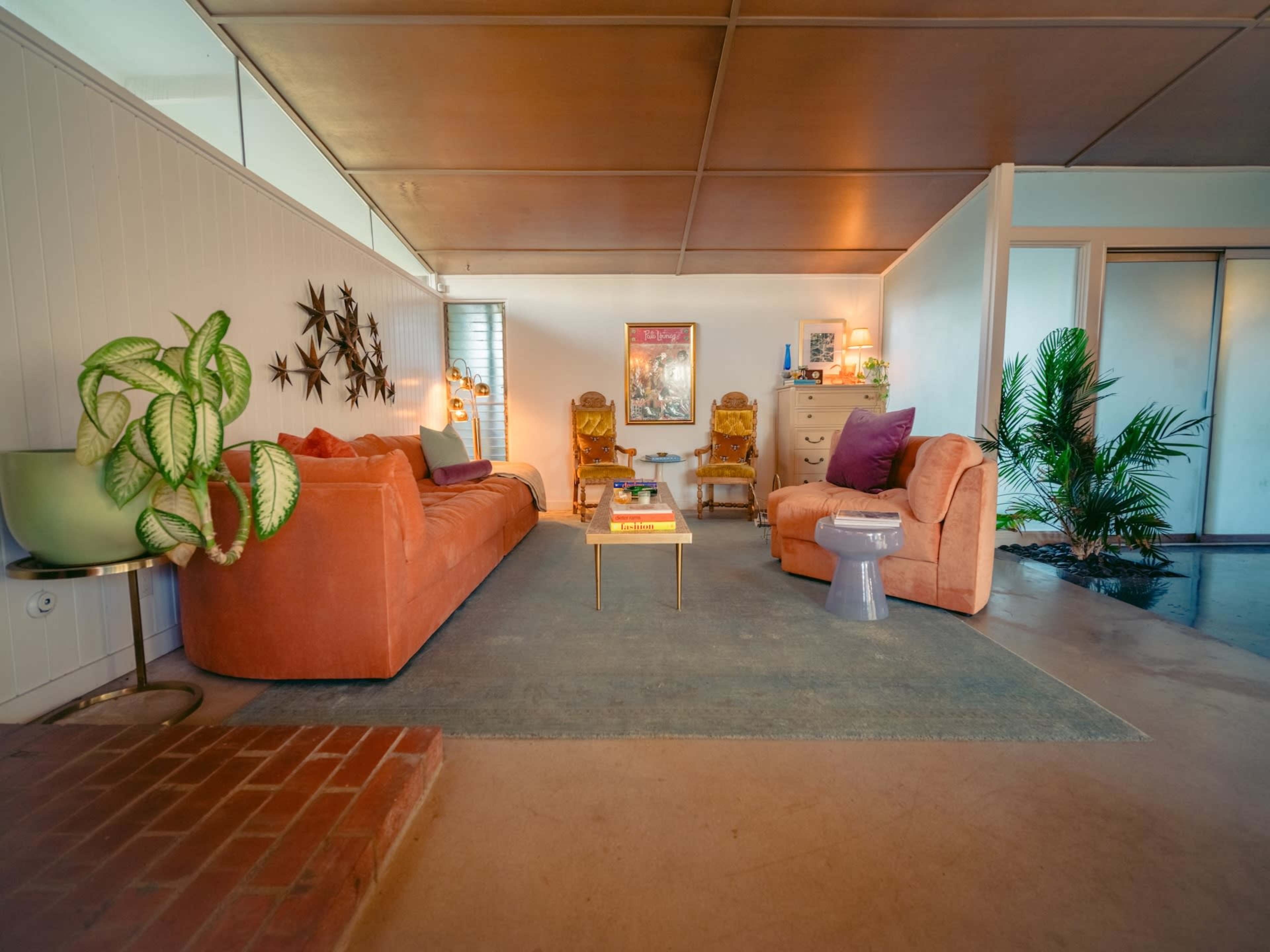 The image shows a modern living room featuring a coral-colored sofa, a small coffee table, and various decorative elements including plants and artwork.