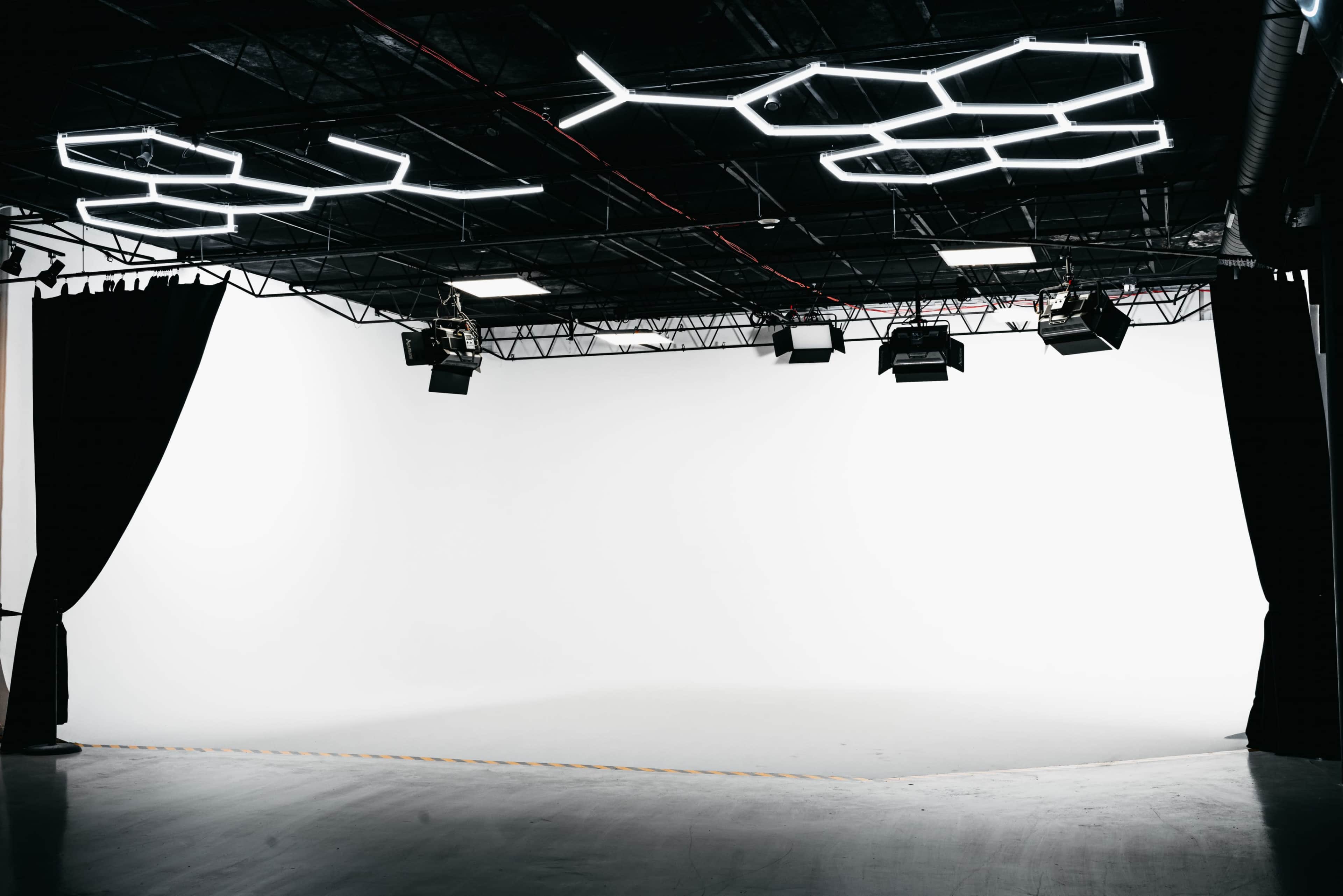 A spacious studio with a clean white backdrop, dim lighting, and modern overhead lighting fixtures.