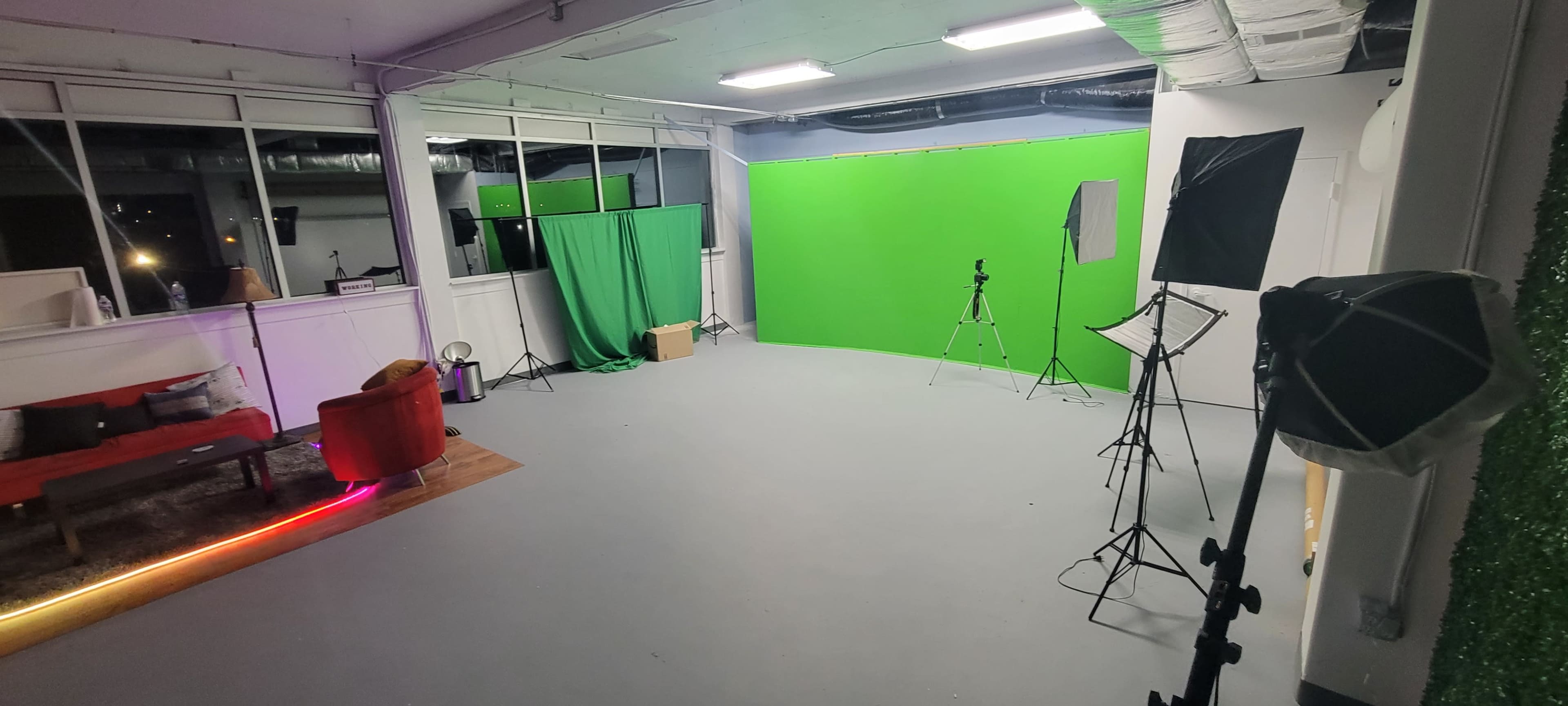 A photography studio with a gray floor, green backdrop, lighting equipment, and a seating area.