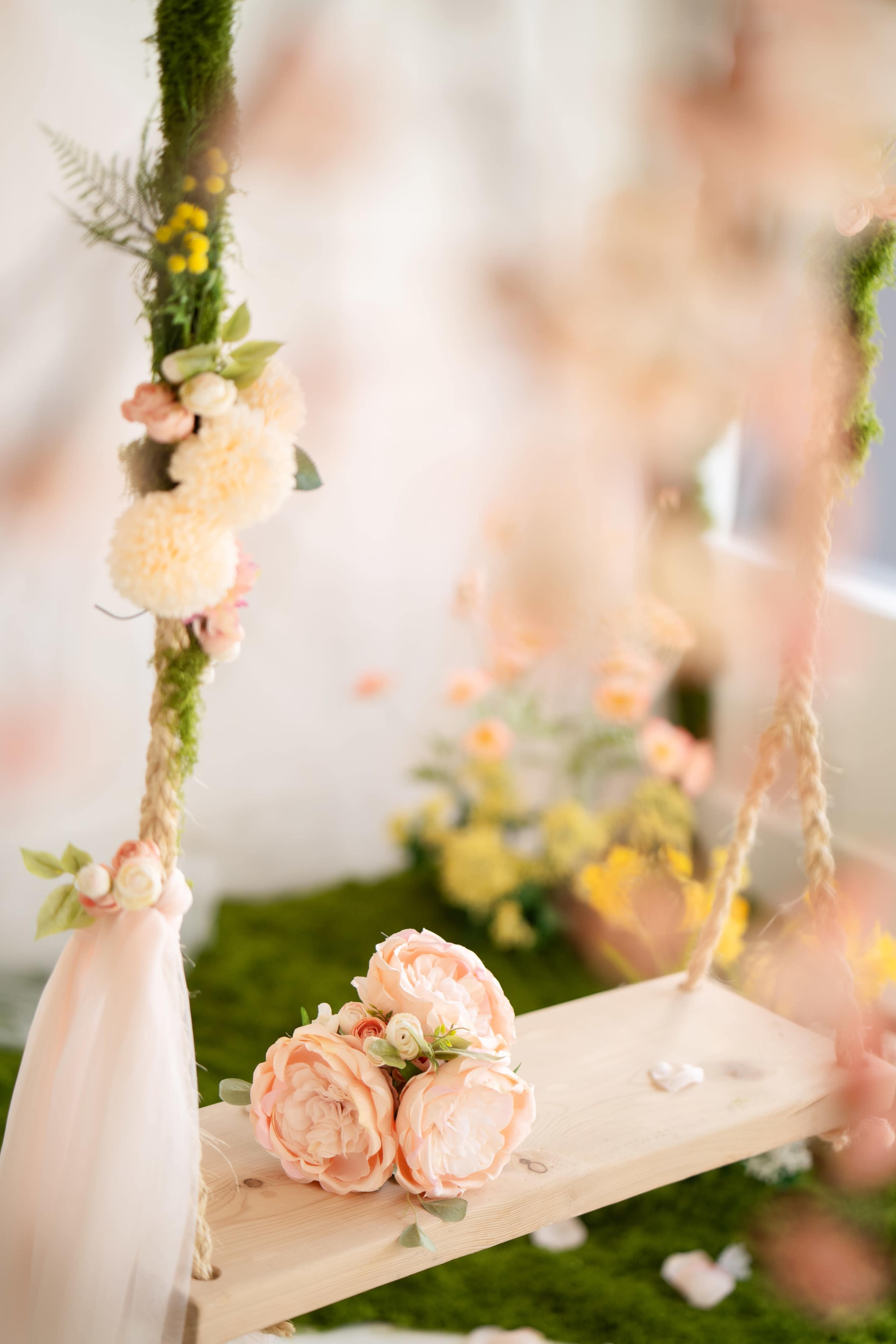 A wooden swing adorned with floral decorations sits on a grassy surface surrounded by various colorful flowers.
