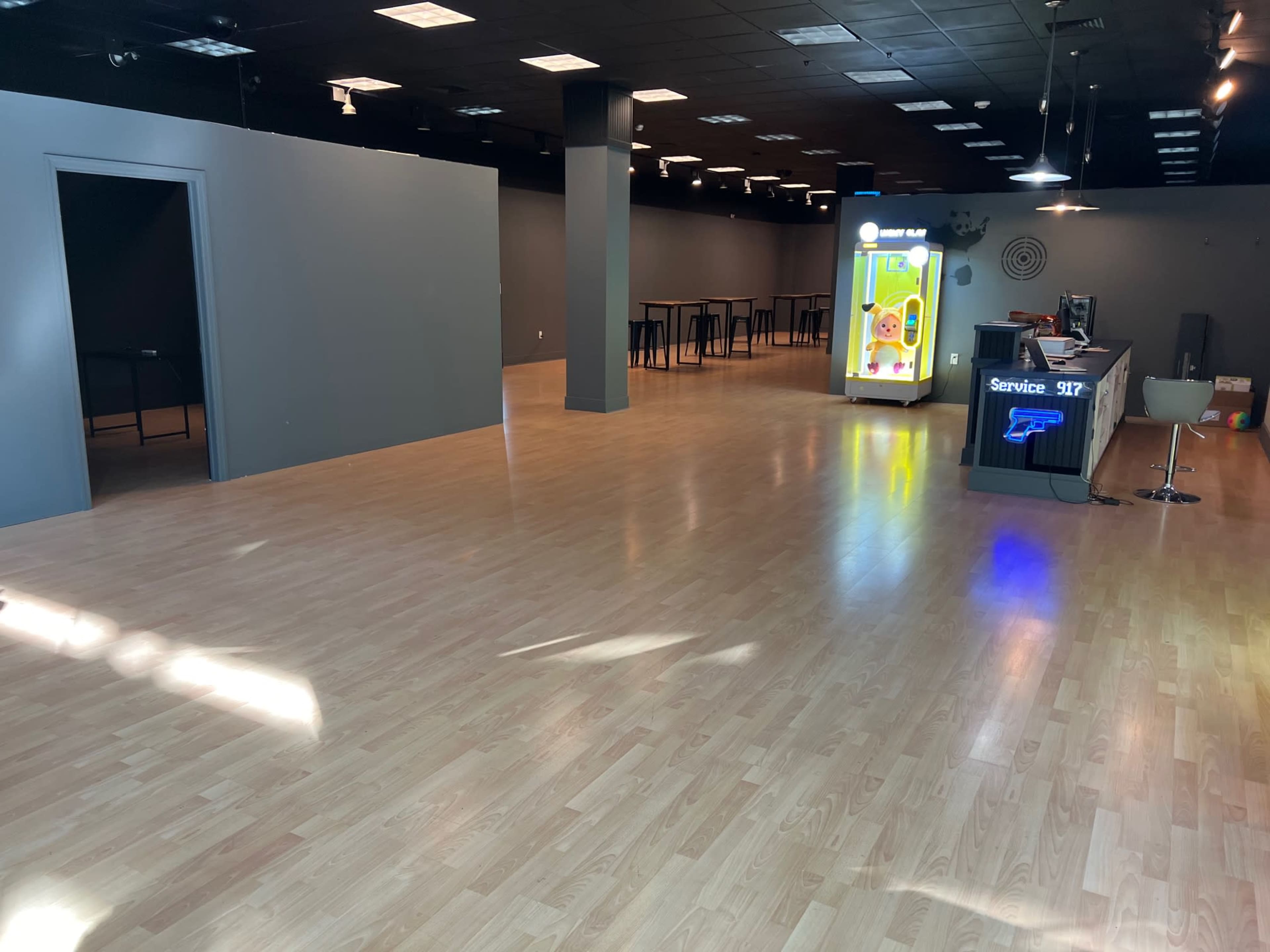 The image shows a spacious, empty interior of a commercial space with hardwood flooring, minimal furniture, and a service counter in the foreground.