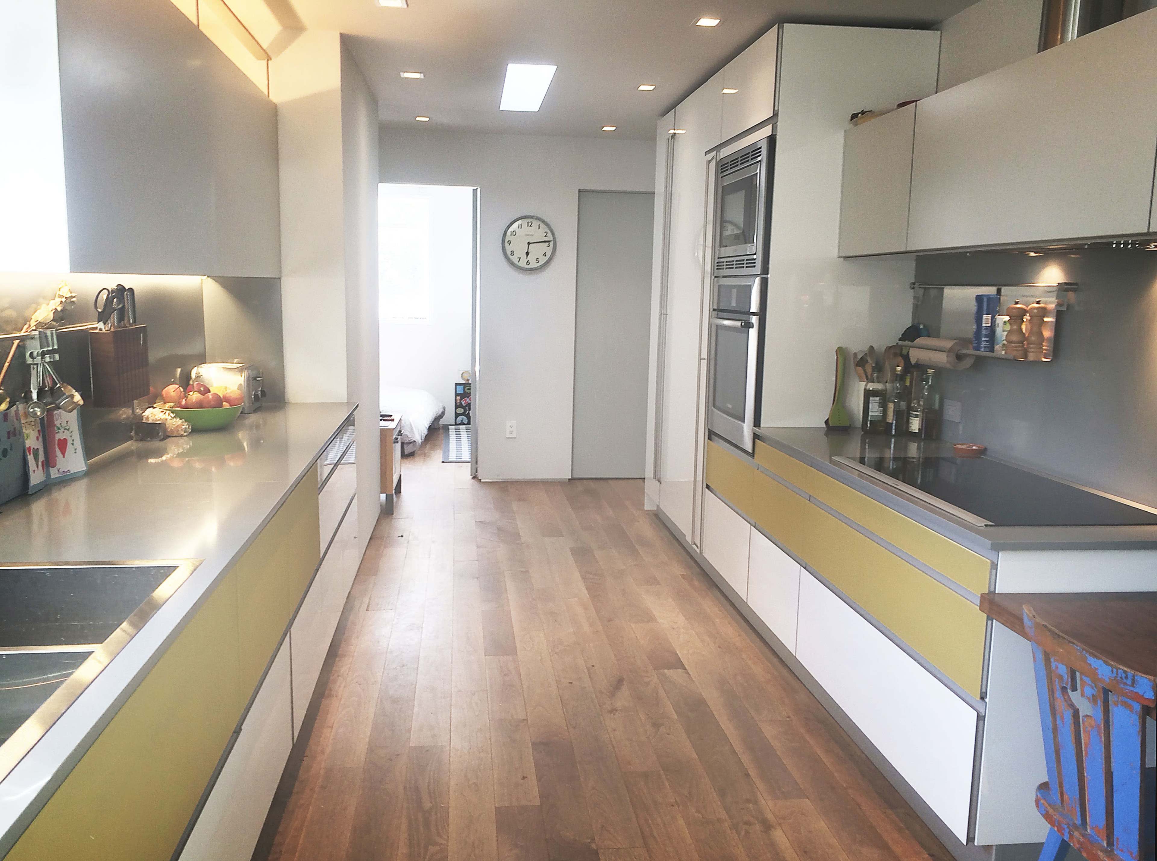 A modern kitchen with yellow accents, hardwood floors, and stainless steel appliances, leading to a doorway that opens into another room.