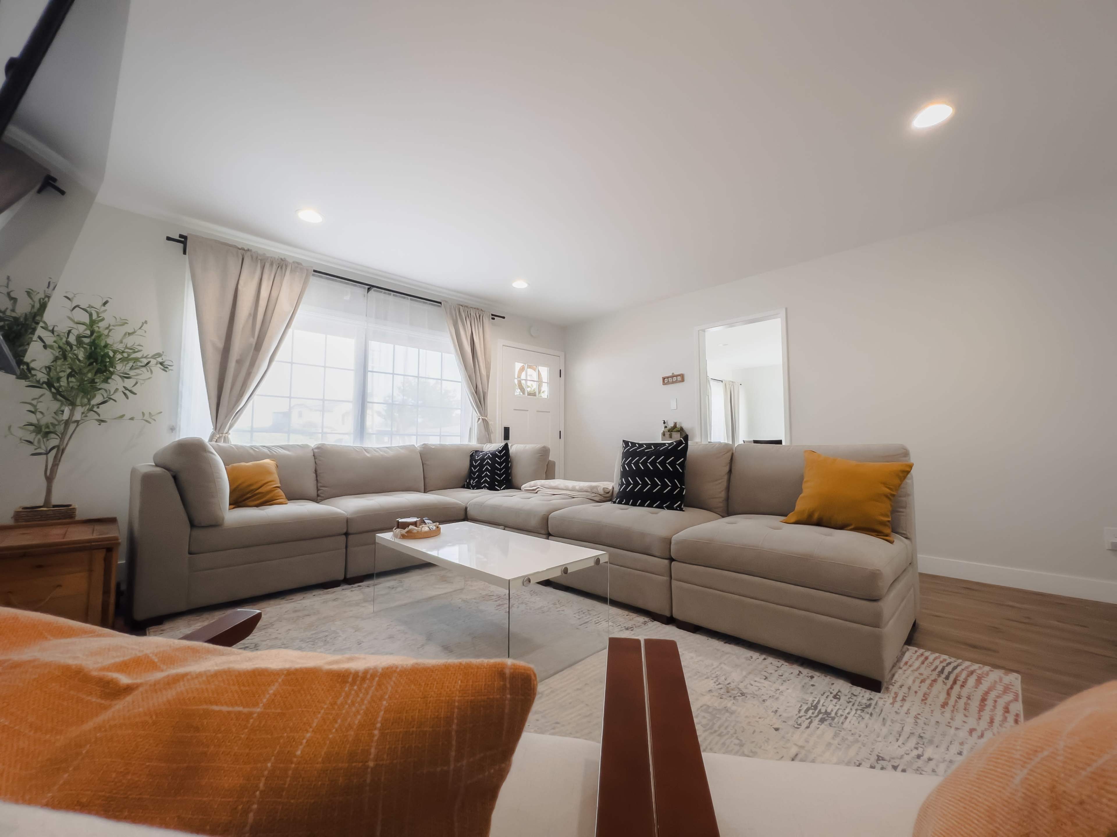 A spacious living room with a sectional sofa, a coffee table, and large windows allowing natural light to enter.