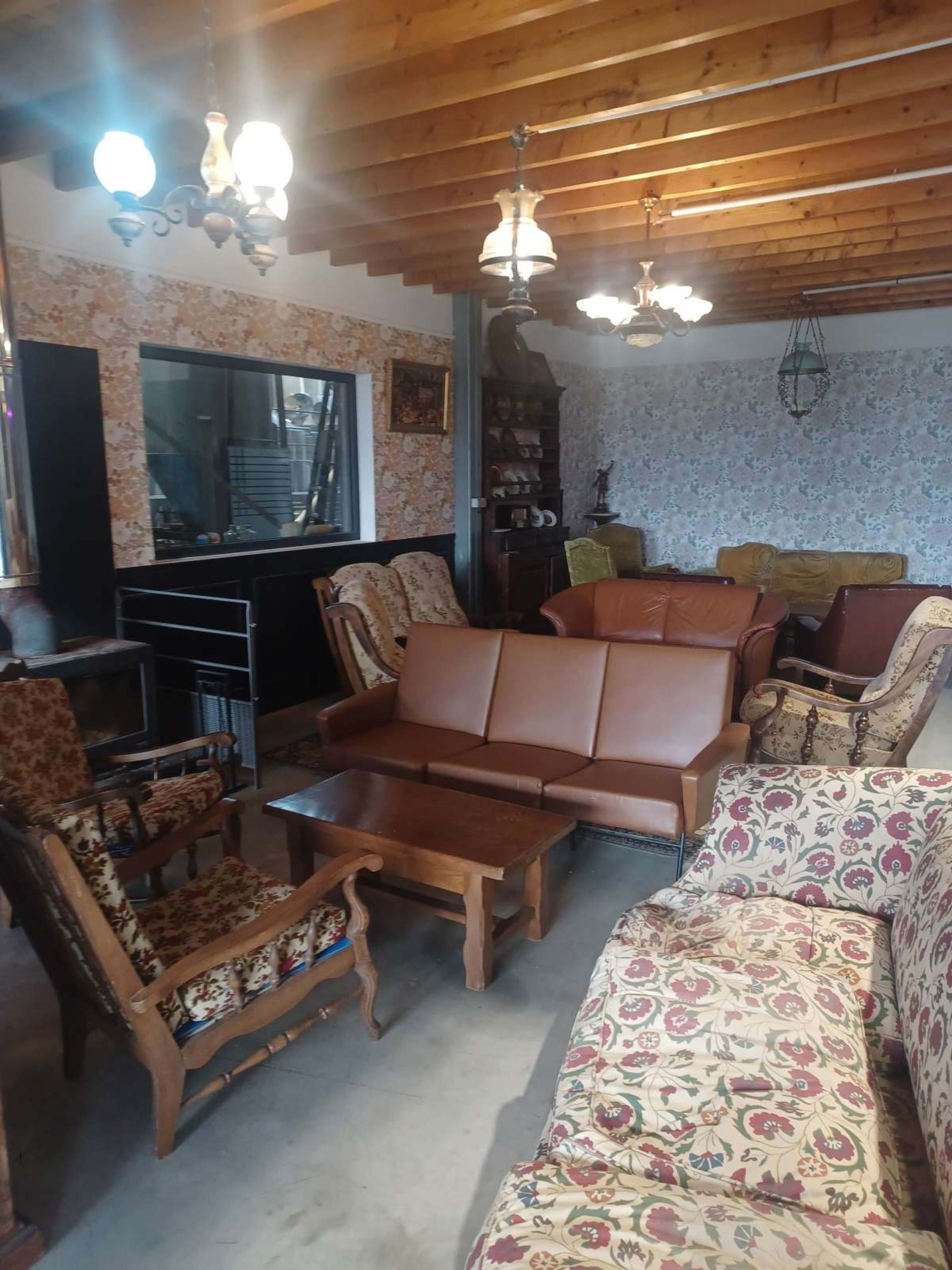 The image shows a cozy living room with various styles of seating arranged around a wooden coffee table, featuring a mix of patterned upholstery and wooden accents.