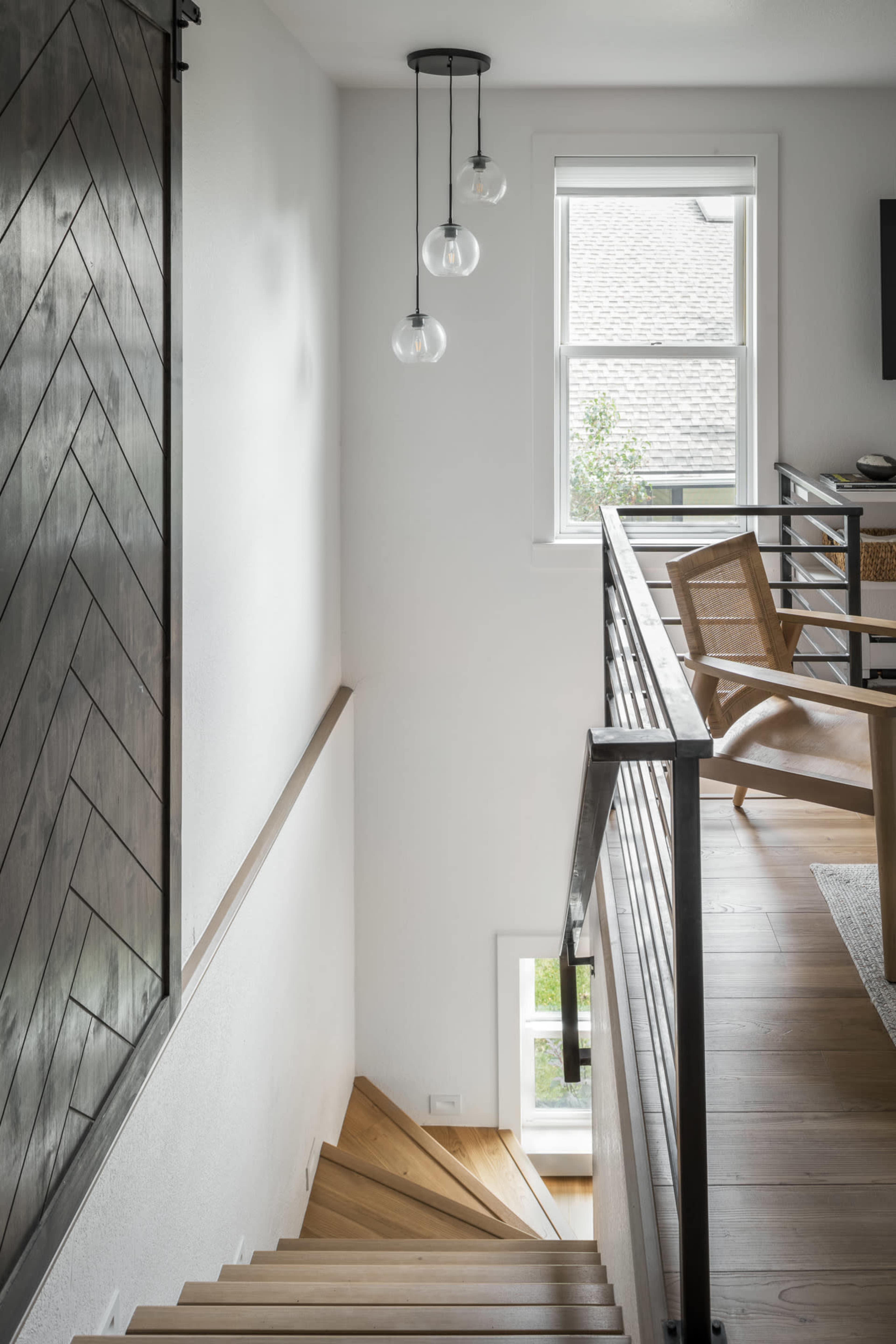 A staircase leads down from a second-floor landing, featuring a wood railing and modern lighting fixtures above.