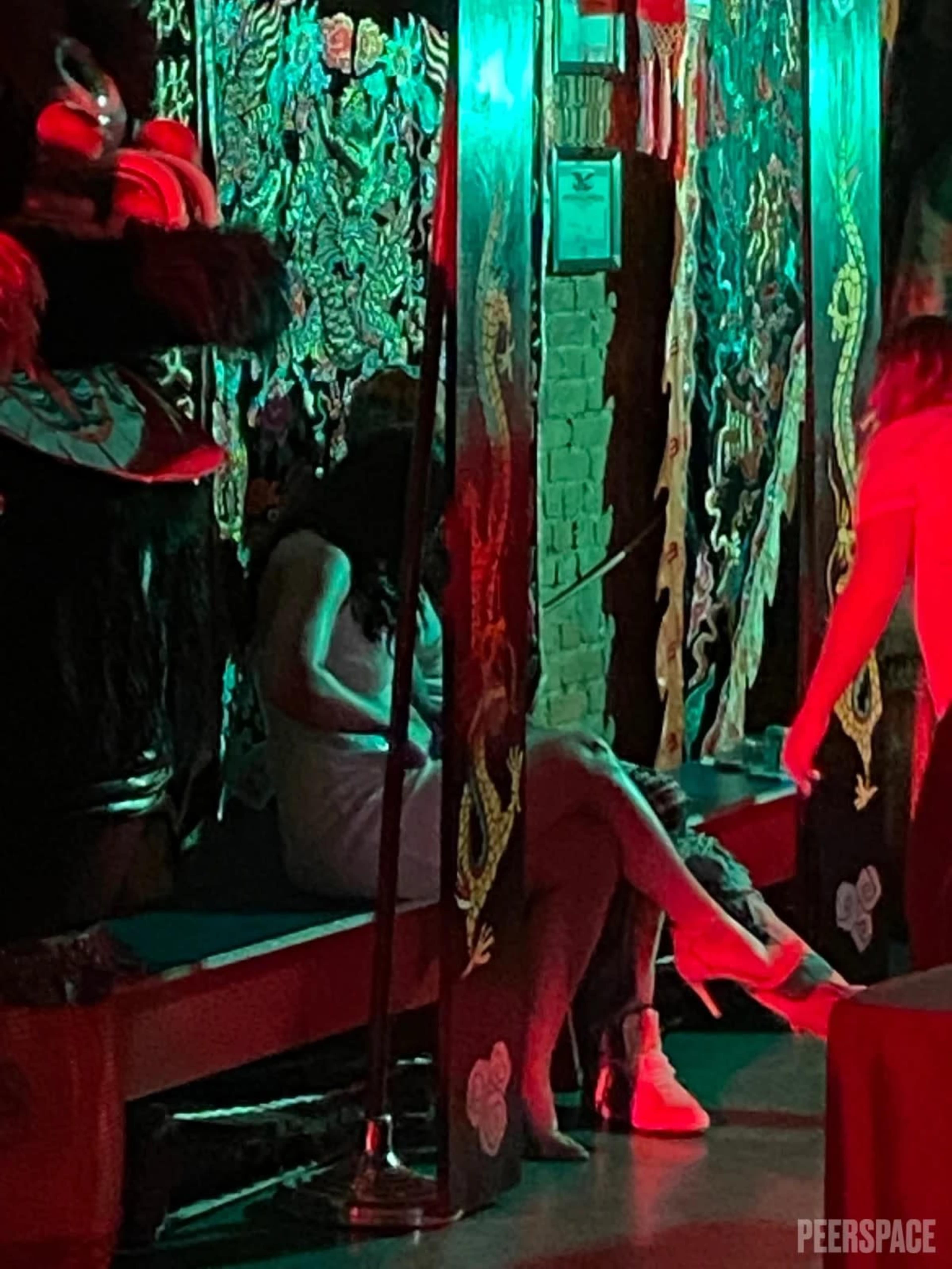 The image shows a dimly lit room decorated with intricate tapestries, where two individuals are seated close together on a bench.