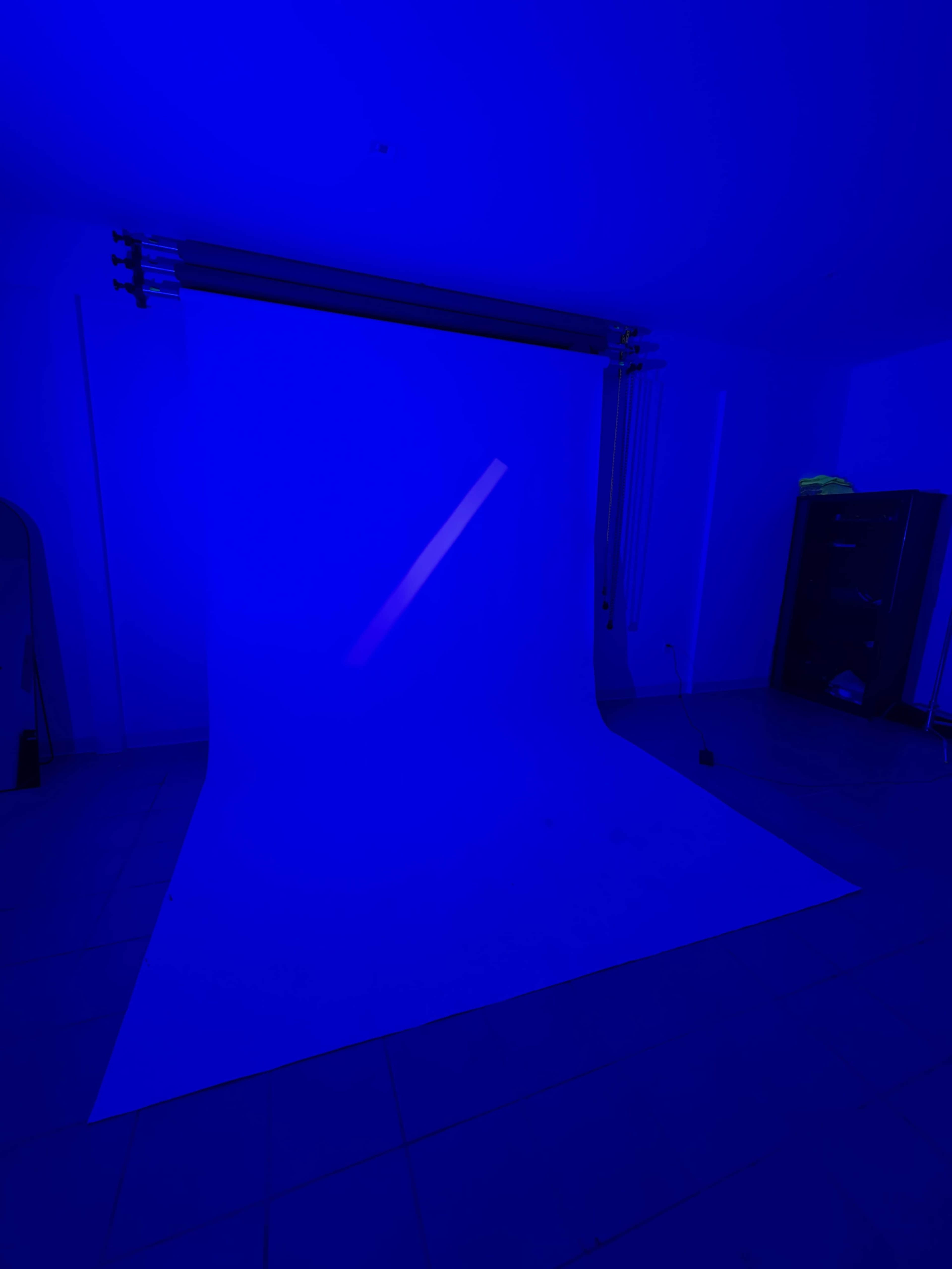 The image shows a photography studio with a blue light illuminating a blank white backdrop.