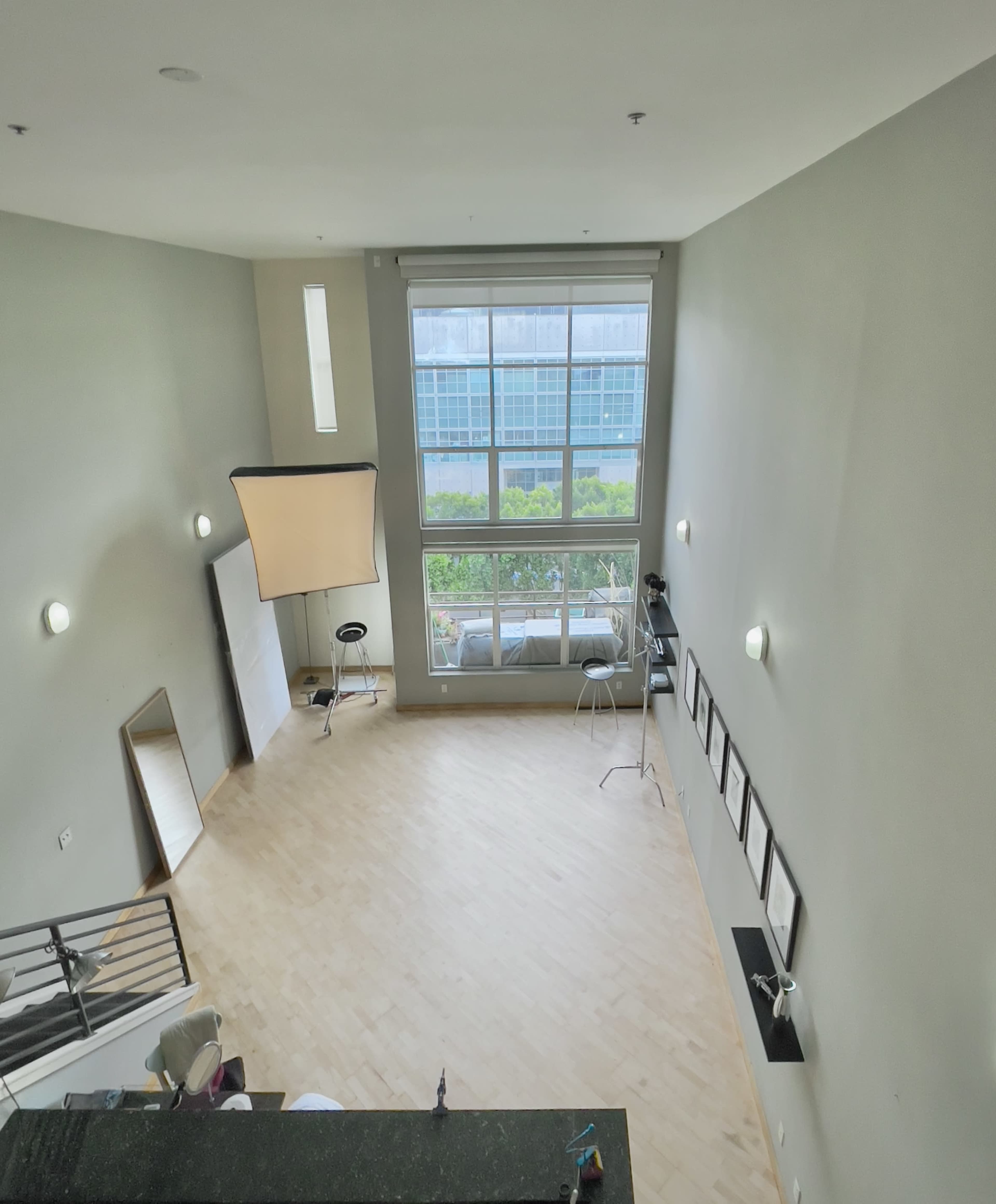 A spacious, well-lit interior room with large windows, a wooden floor, and several pieces of photography equipment set up.