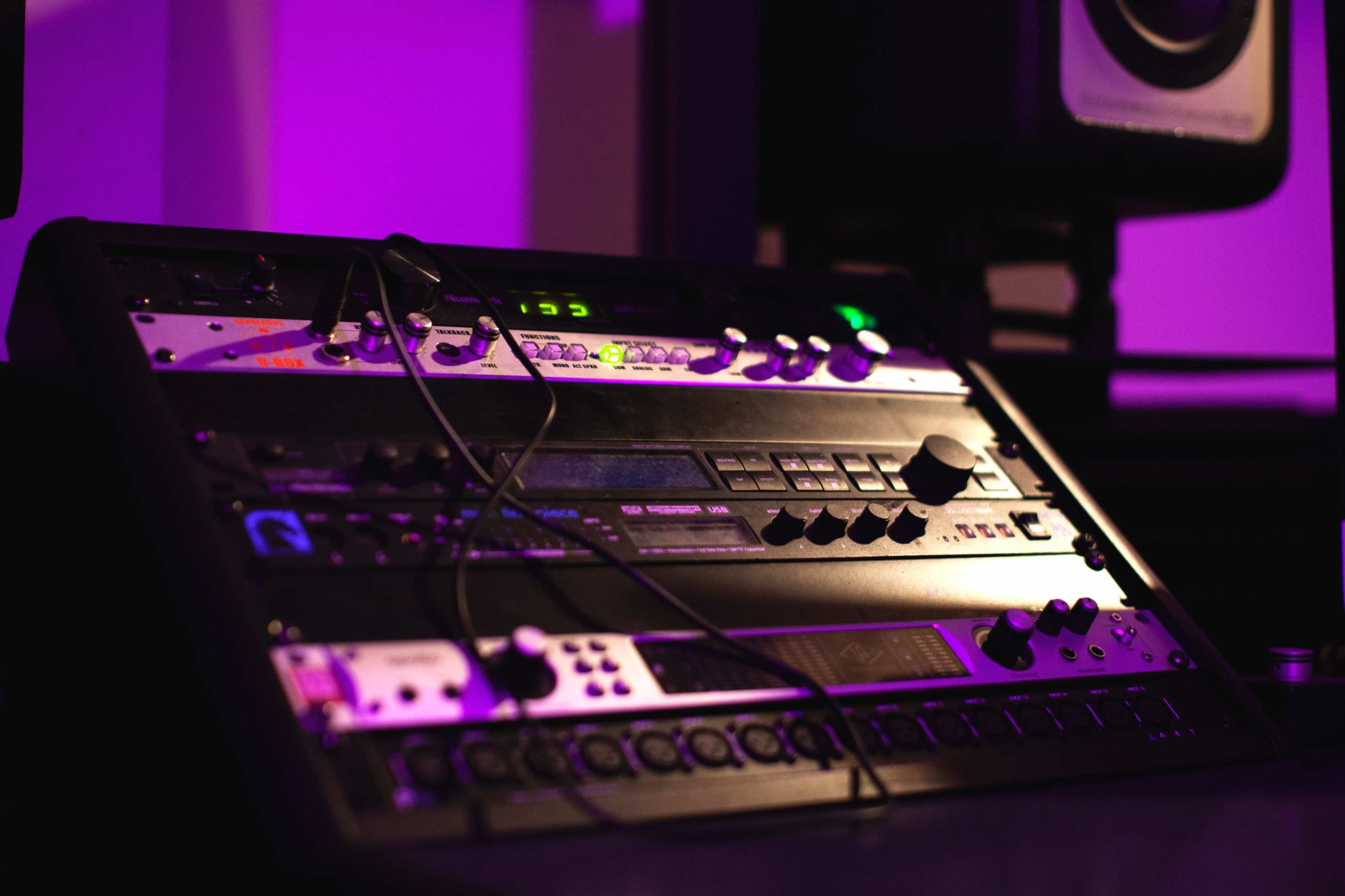 A rack of audio equipment with various knobs and lights is positioned in a dimly lit studio.