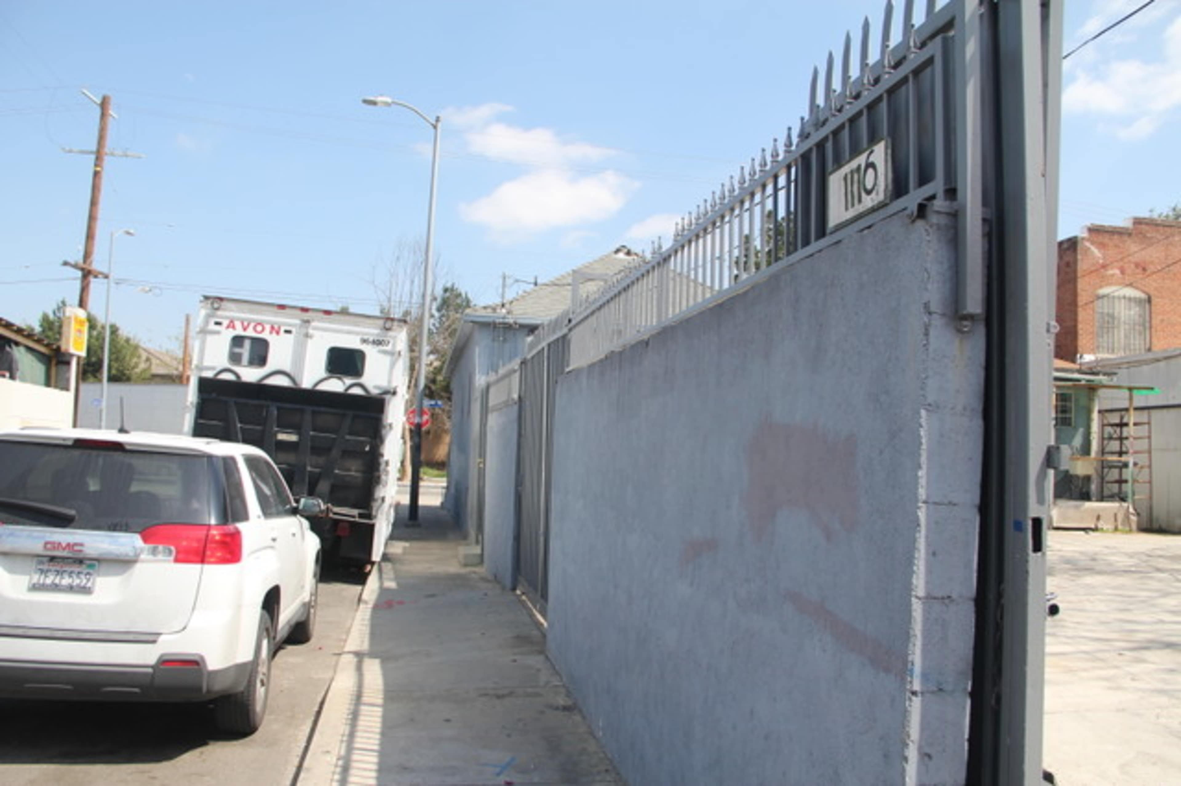 A white vehicle is parked on the side of a street next to a gray concrete wall, with a truck parked partially beyond the wall.