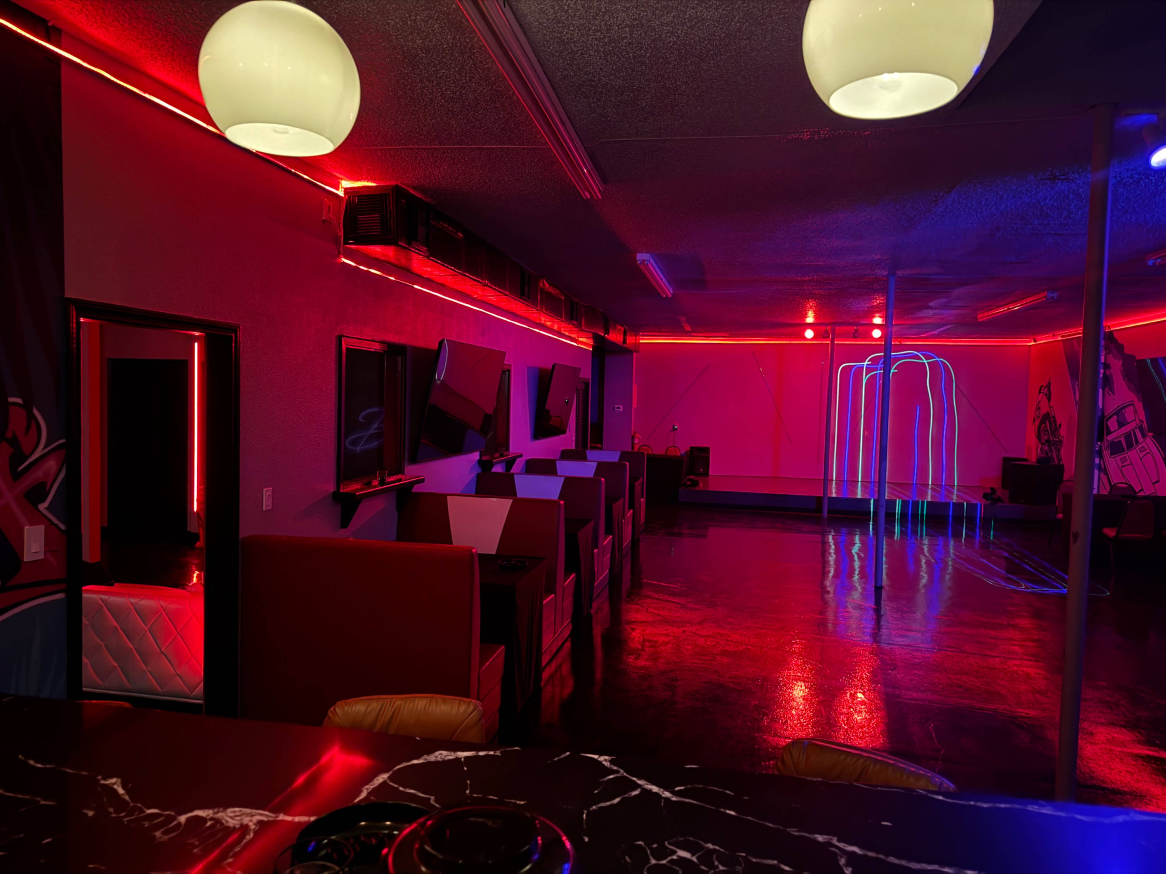 The interior features a dimly lit space with red and blue neon lights illuminating booths and a central area.