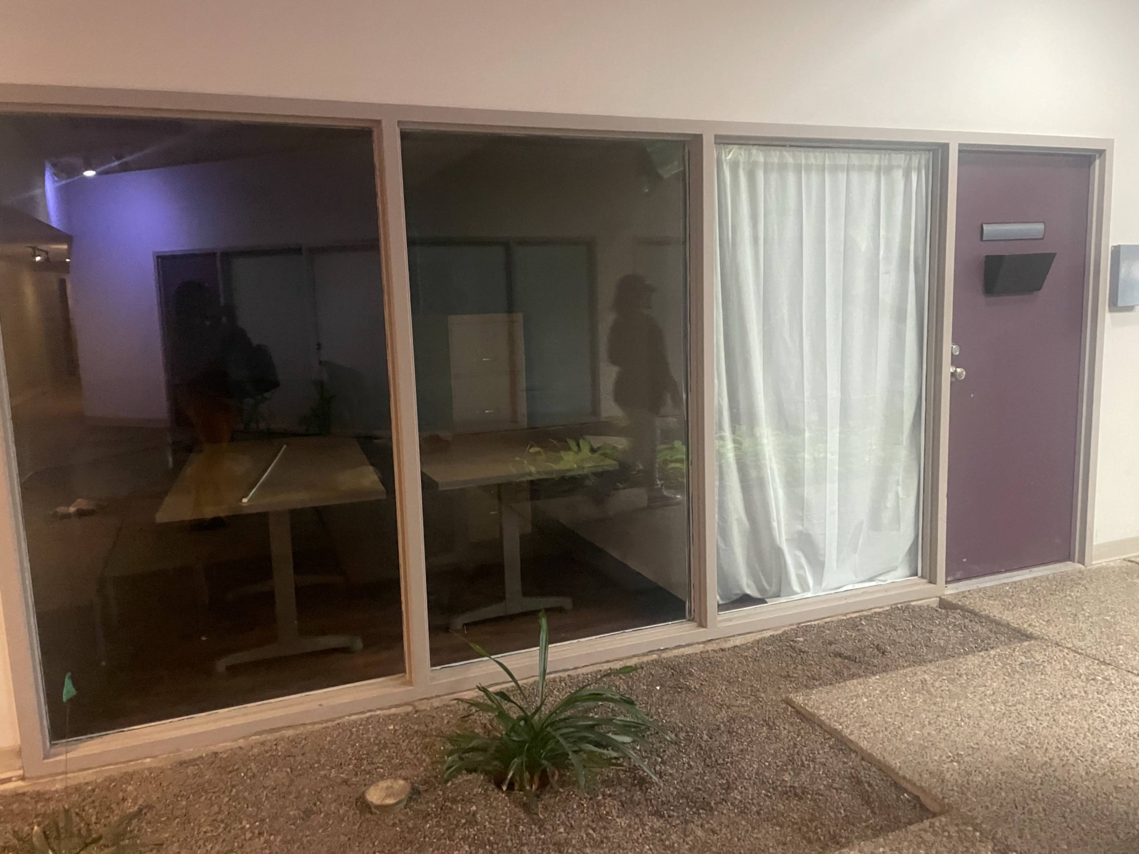 A modern entrance to a building with large windows, a sheer curtain, and a simple door beside a gravel walkway.