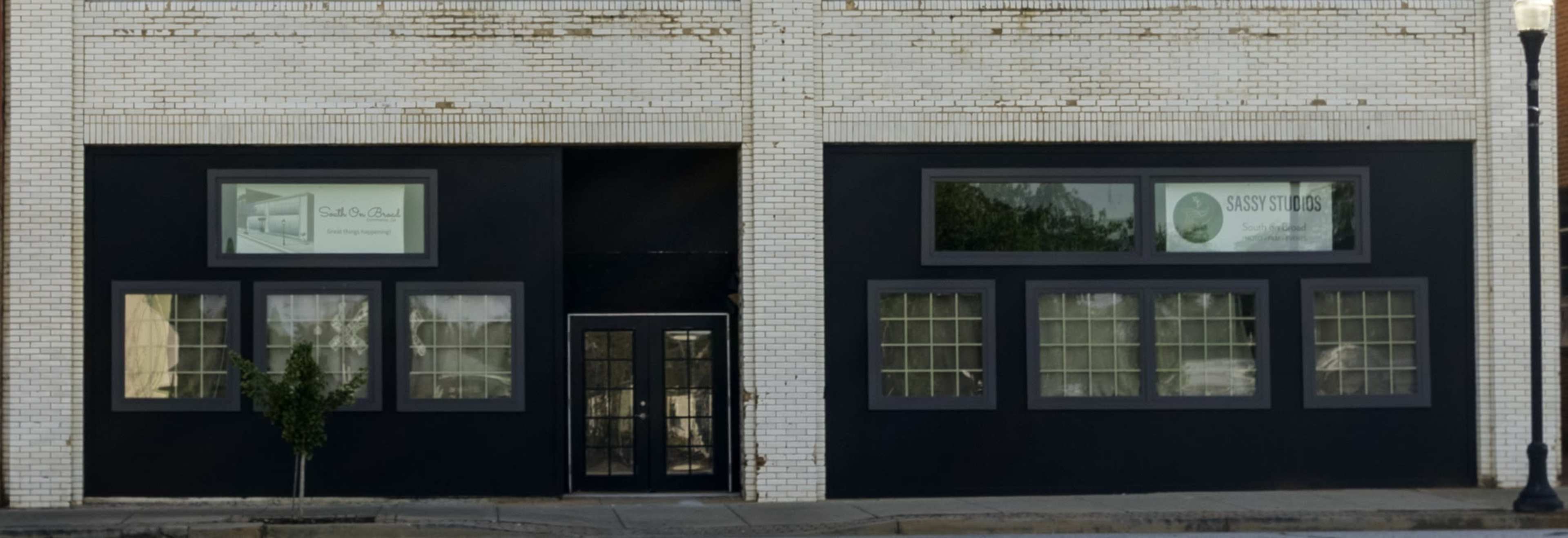 A brick building with a black facade and large windows, including two display windows on either side of a central door.