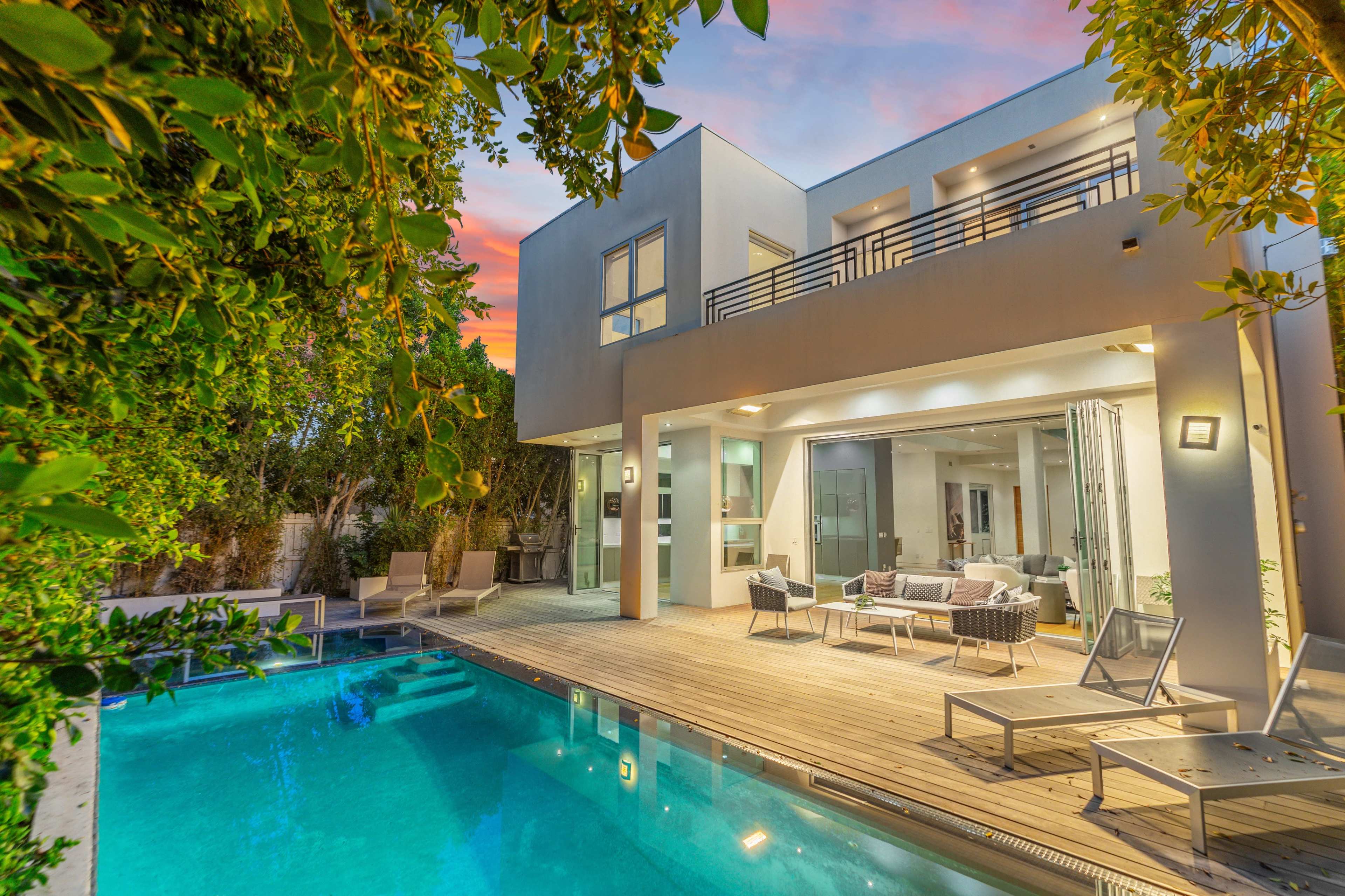 A modern house with a swimming pool and outdoor seating area is surrounded by lush greenery.