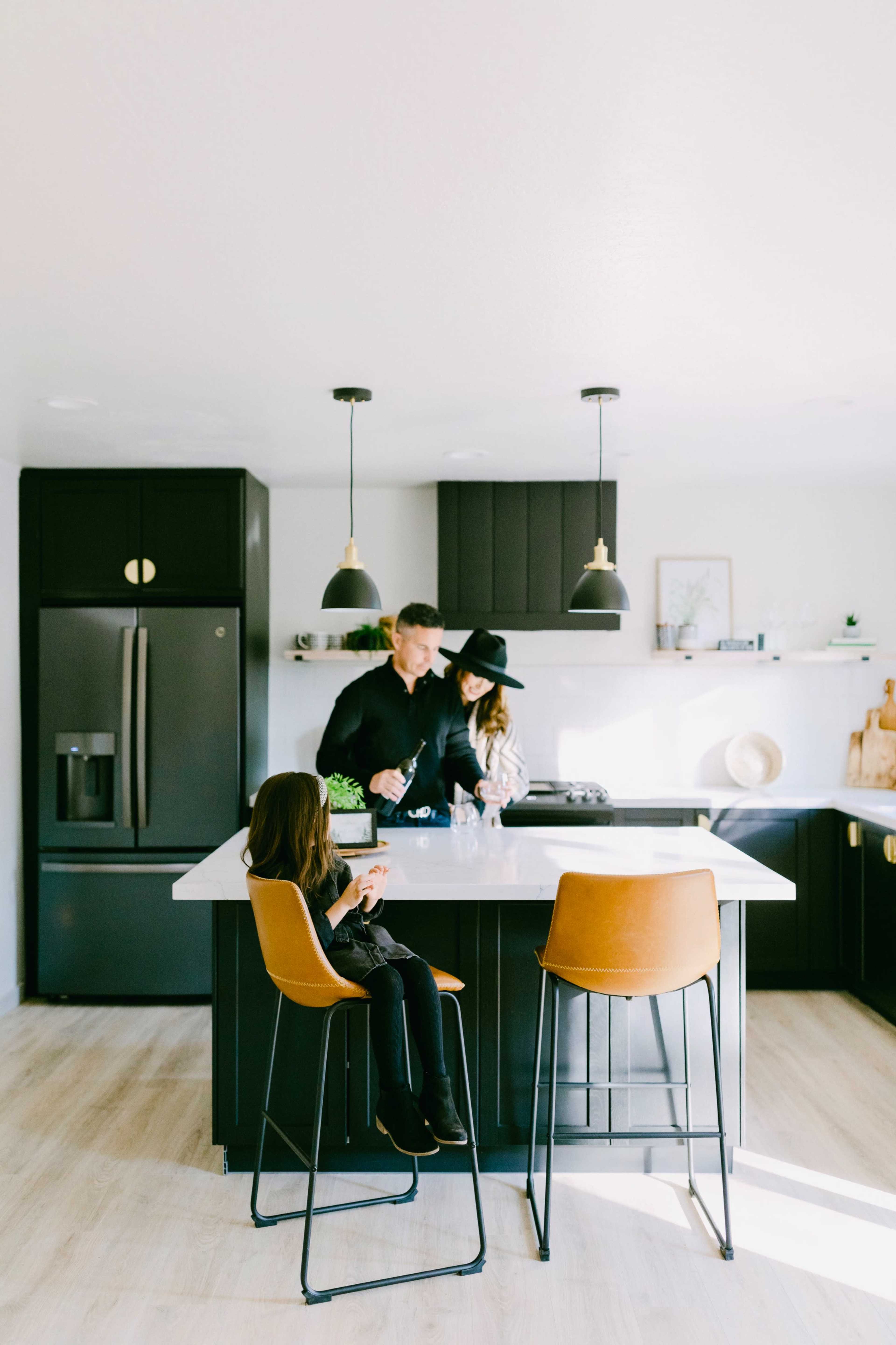 A family prepares food together in a modern kitchen with dark cabinetry and a light countertop.