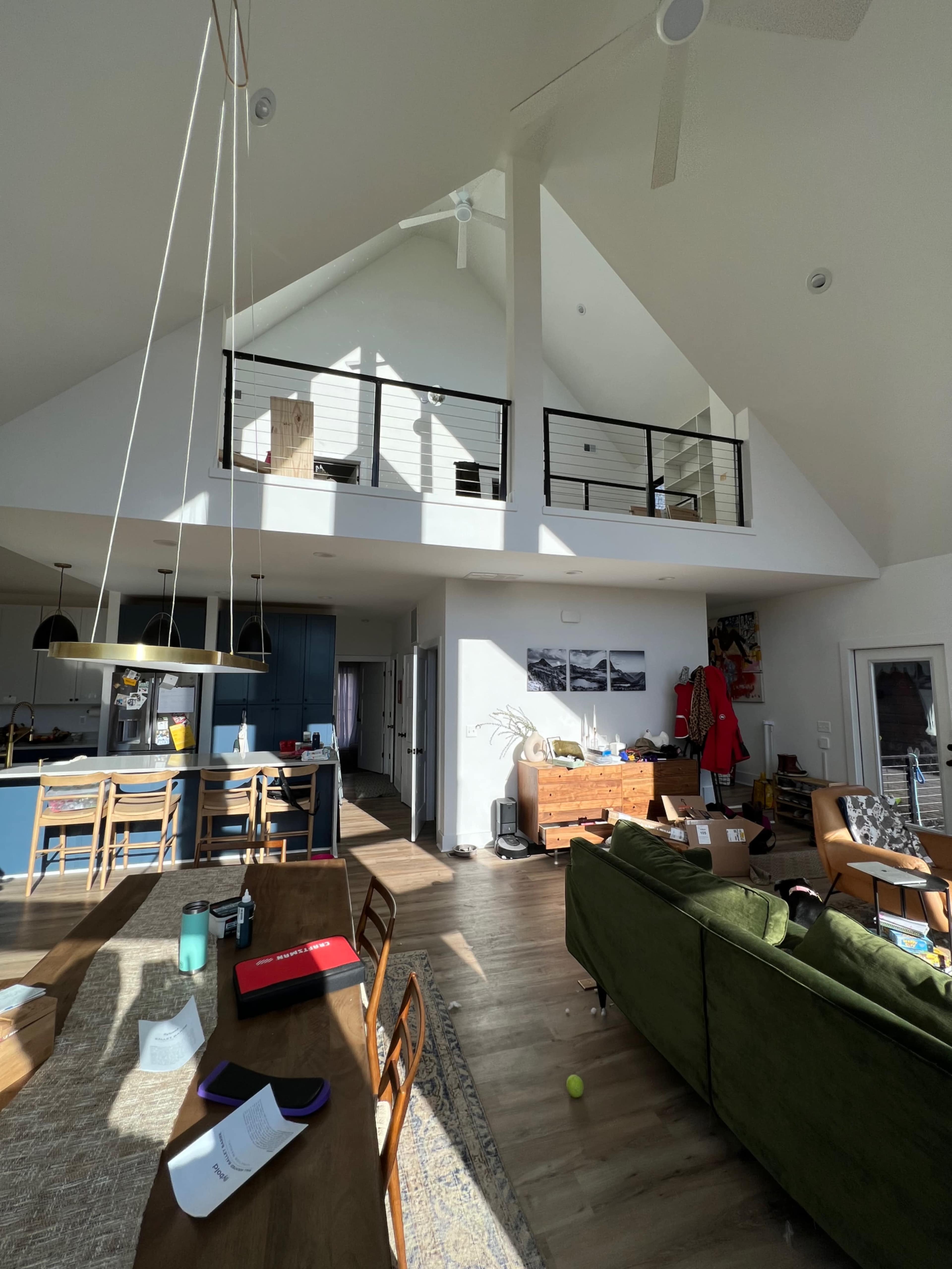 The image shows a spacious, modern living area with high ceilings, large windows, and a lofted second level.