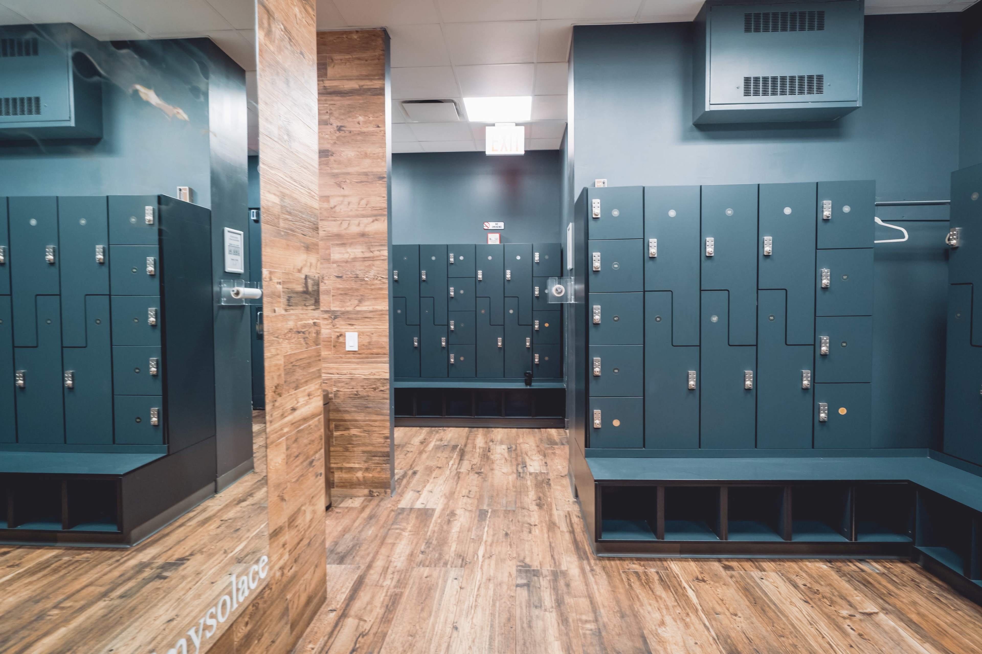 A locker room with dark green lockers arranged along the walls and a wooden accent wall.