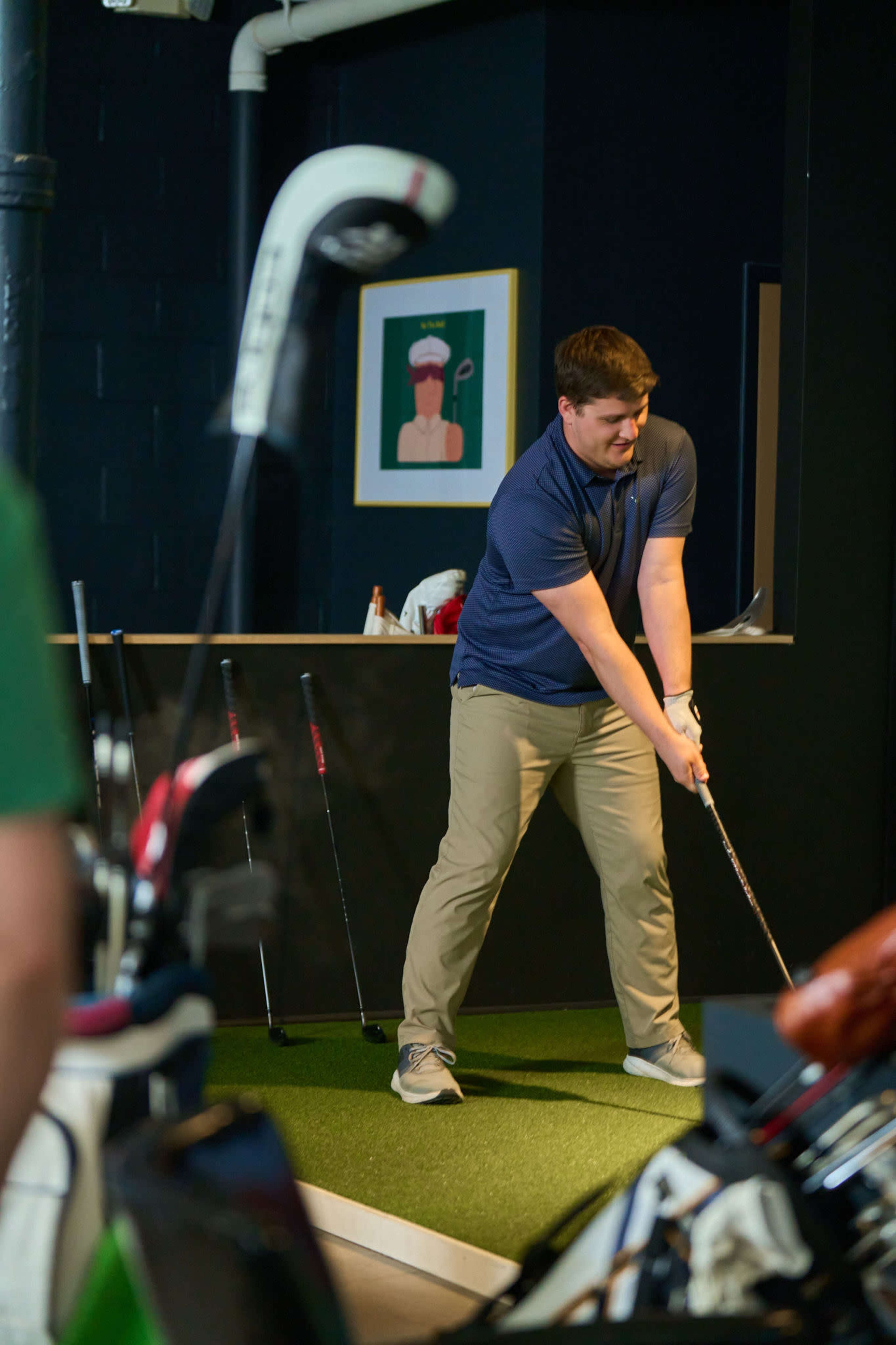 A man dressed in a blue shirt and beige pants prepares to swing a golf club in a simulated golf environment.