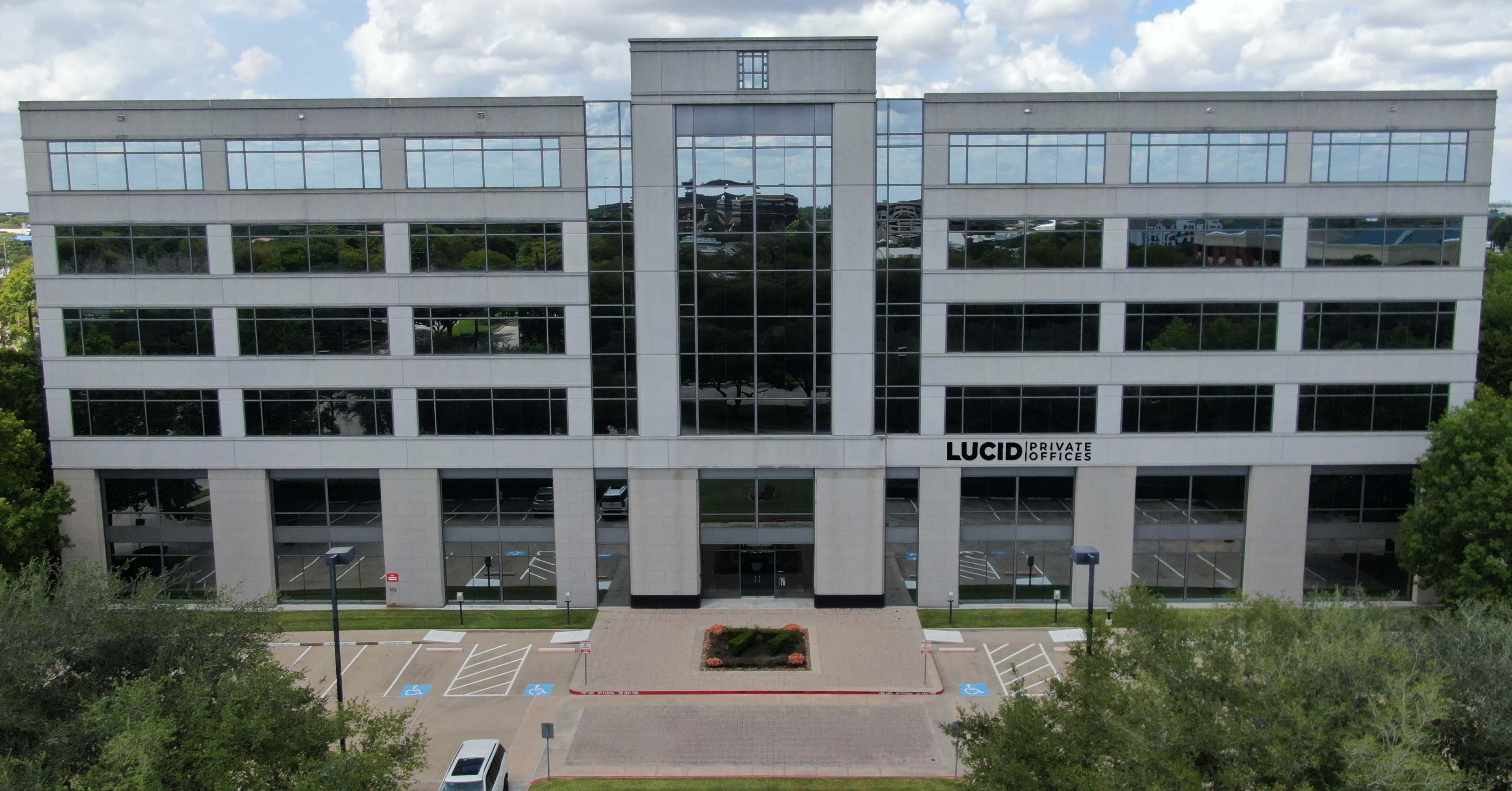 The image shows a modern office building with large glass windows and a landscaped entrance area, featuring a sign that reads "LUCID PRIVATE OFFICES."