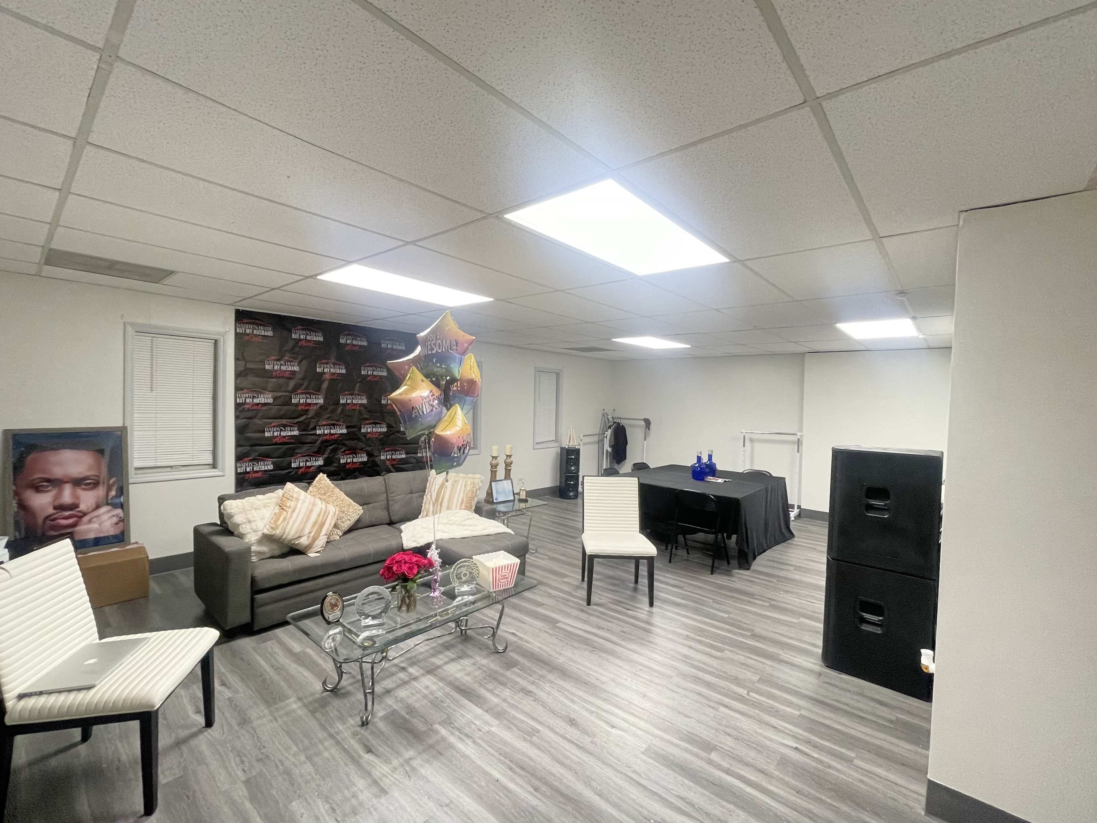 The image shows a spacious basement room with a sofa, a table set for an event, and decorations including balloons and a framed photo on one wall.