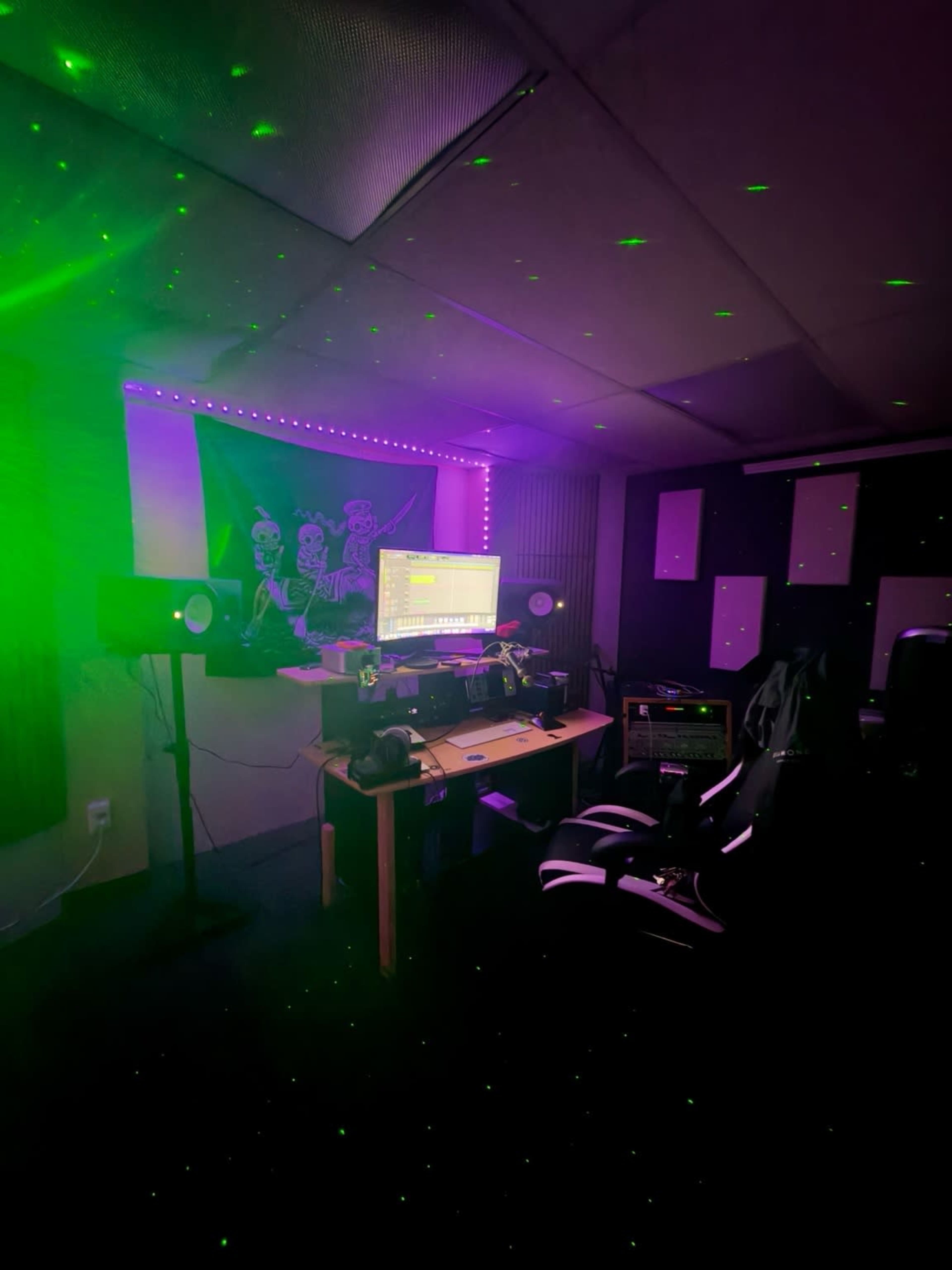 The image shows a music studio with a computer on a table, speakers on either side, and green laser lights illuminating the space.