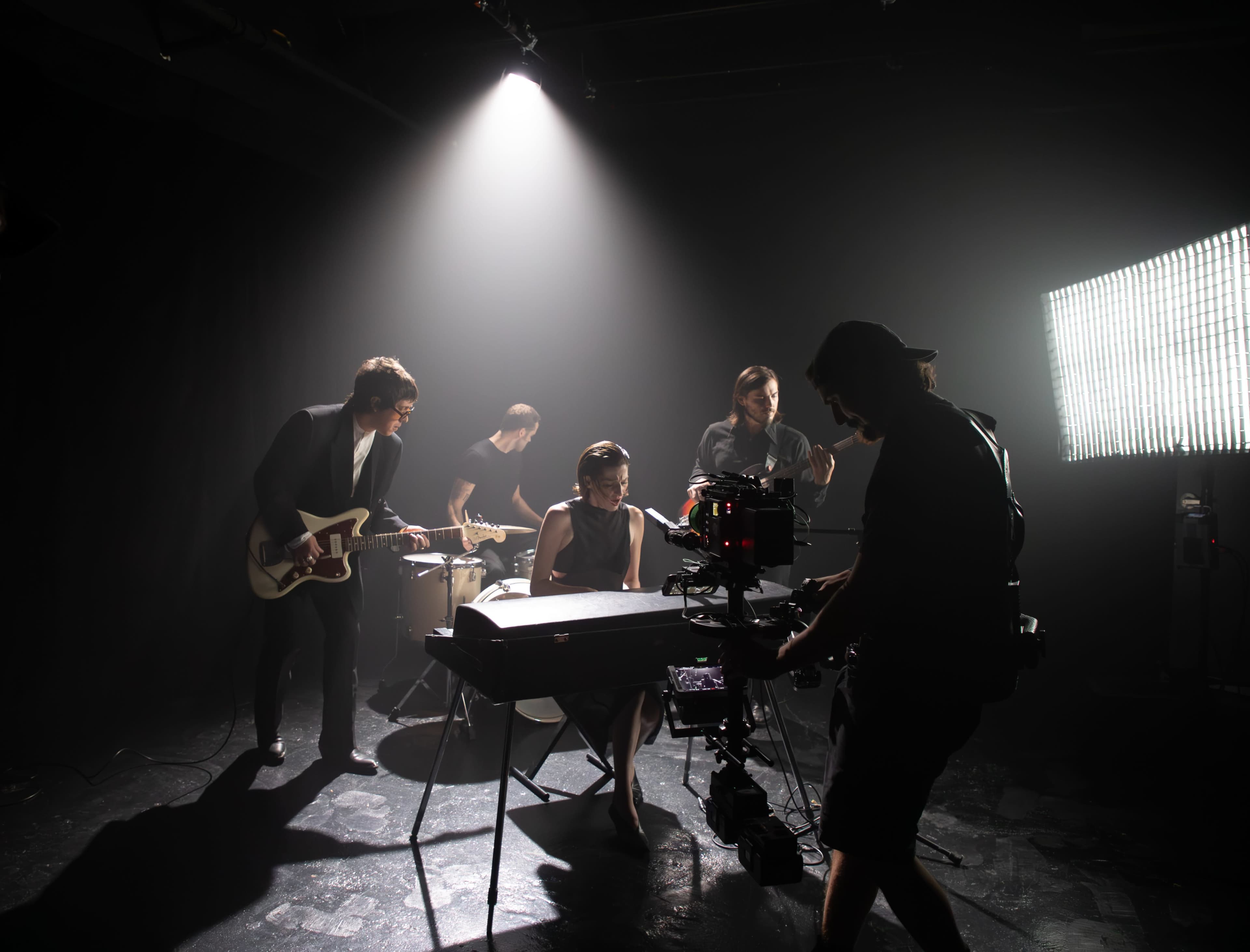 A band performs onstage with a video camera operator capturing the scene under dramatic lighting.