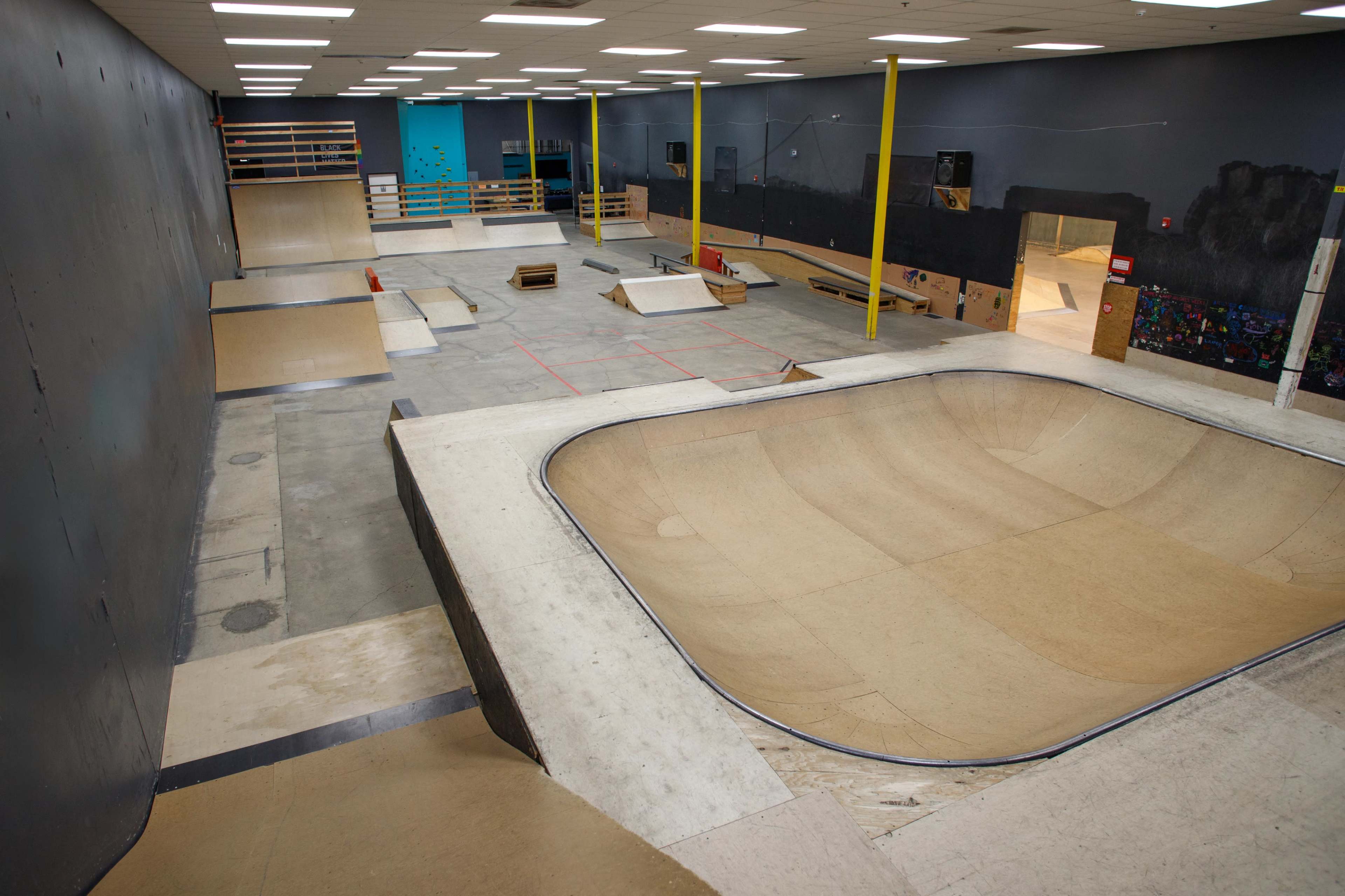 The image shows an indoor skatepark featuring various ramps, a bowl, and a flat area for skateboarding activities.