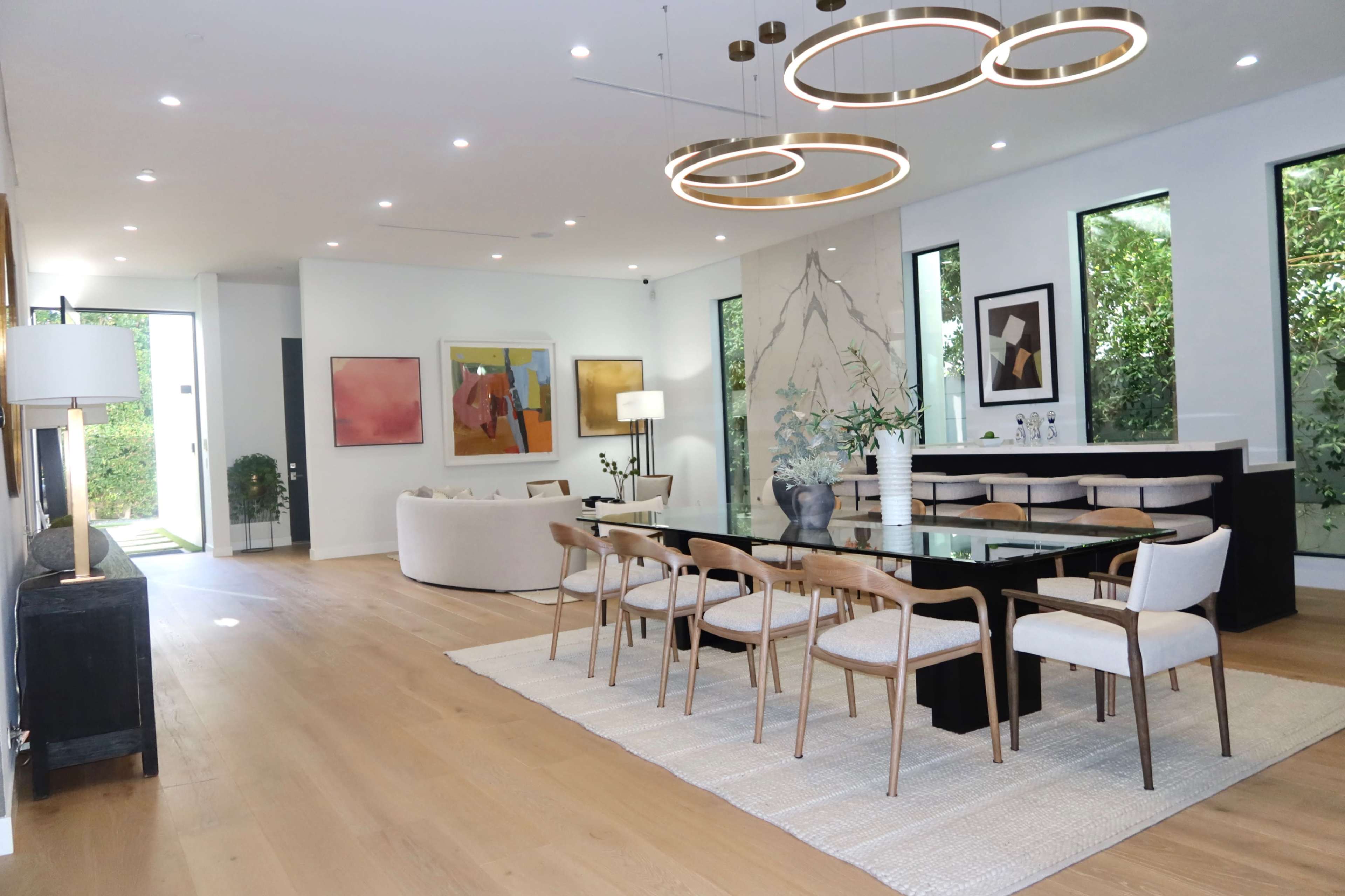 A modern dining area features a long table with eight chairs, large windows, and contemporary artwork on the walls.