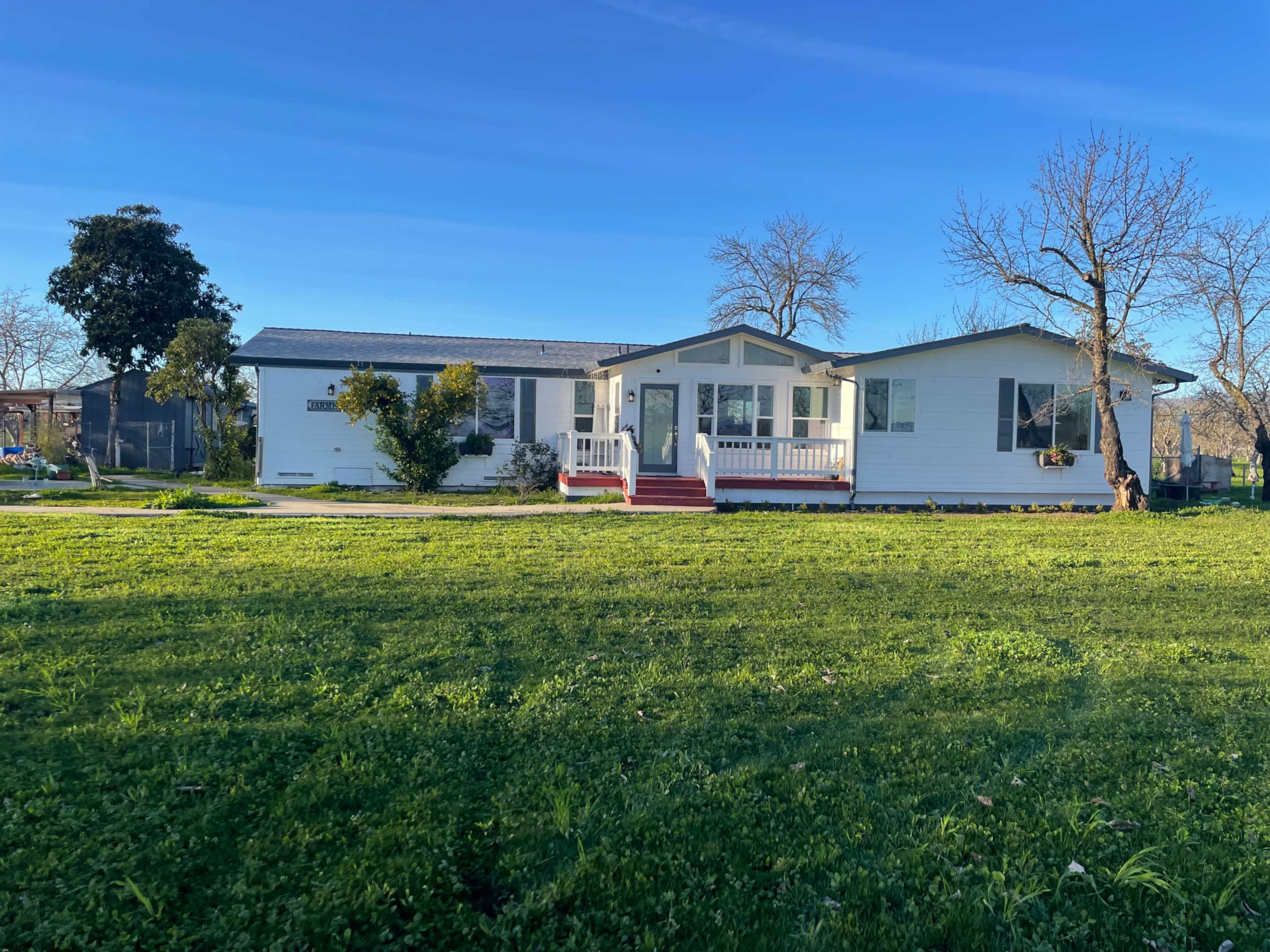 A single-story white house with a front porch, surrounded by green grass and a few trees.