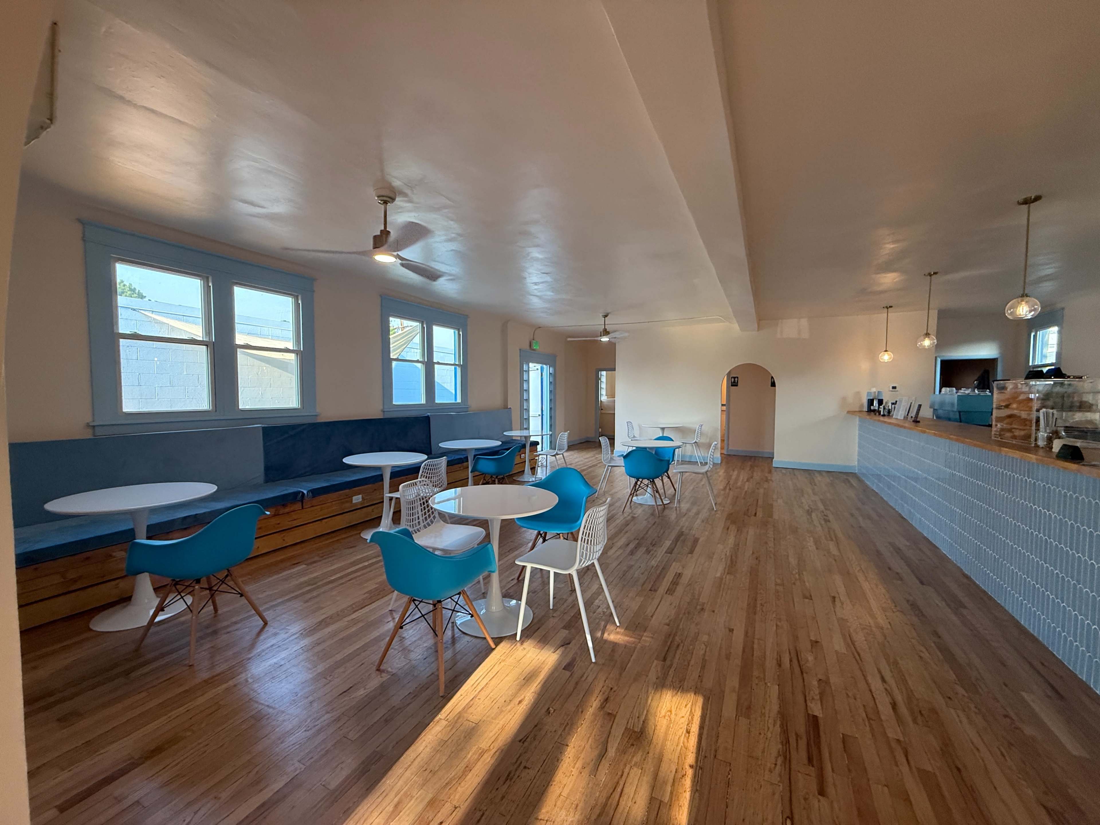 The interior of a spacious cafe features wooden floors, blue accents, and a counter with seating areas.