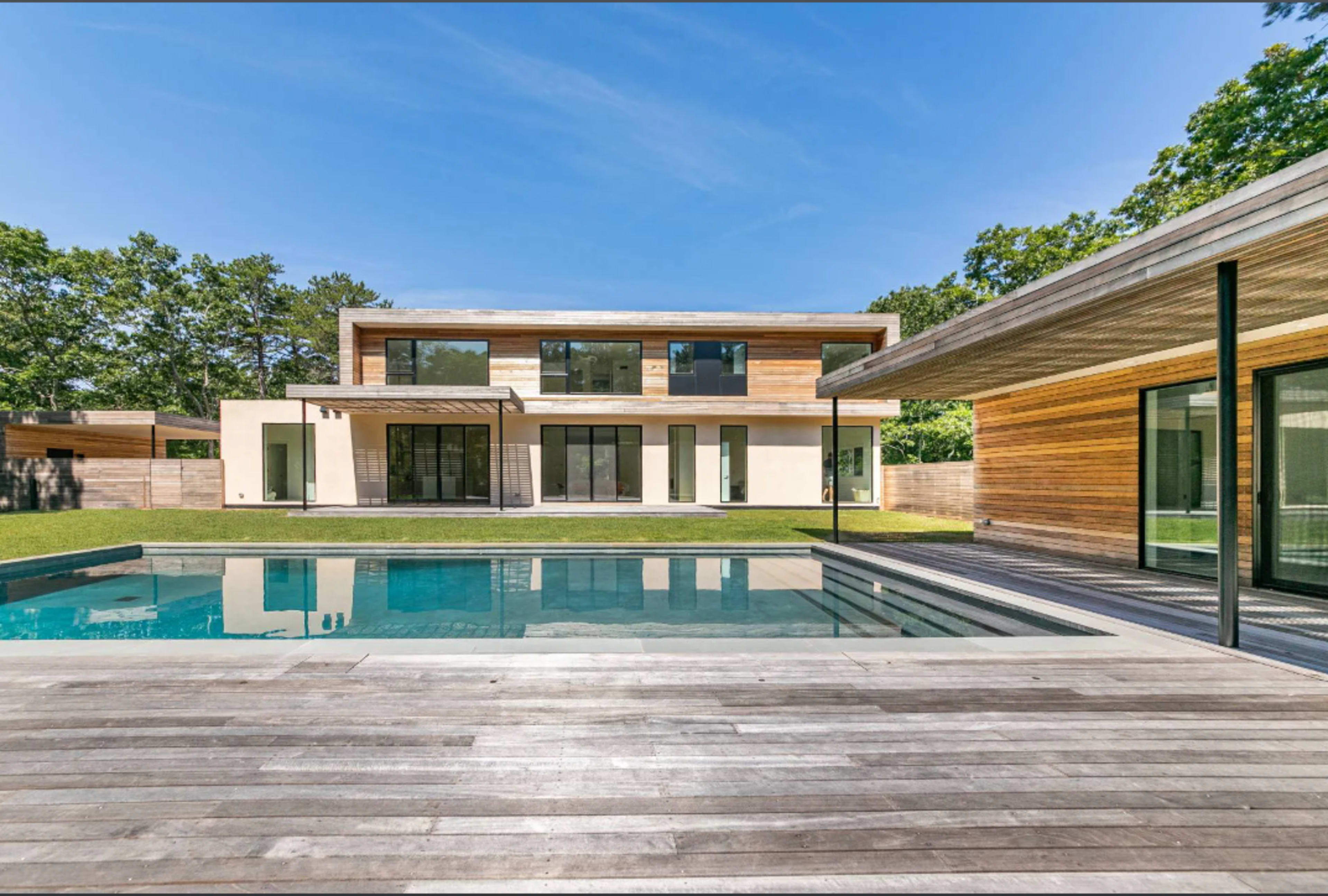 A modern two-story house with a pool is surrounded by greenery and features large glass windows and wooden accents.