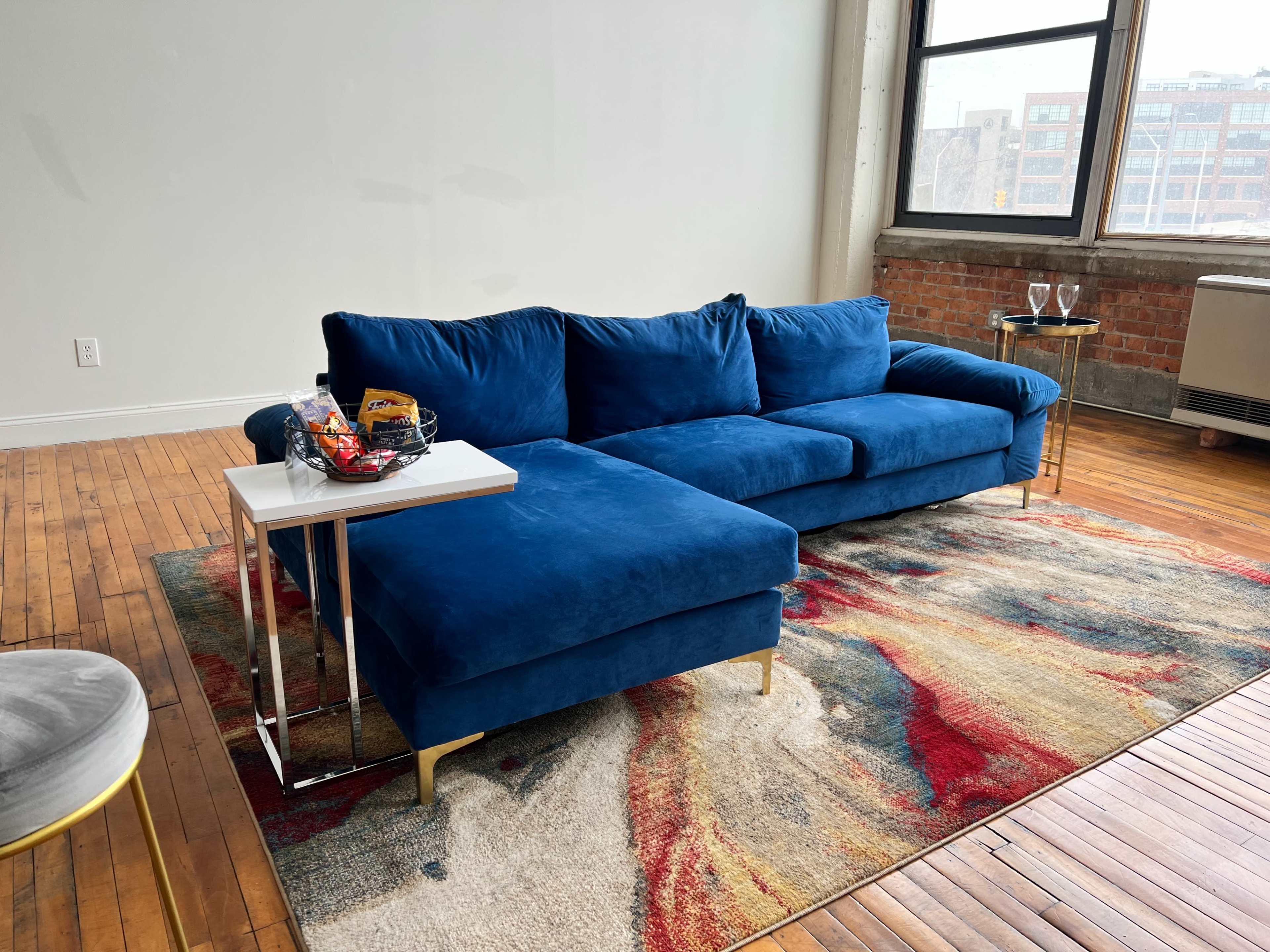 A blue sectional sofa is placed on a colorful rug in a room with large windows and wooden flooring.