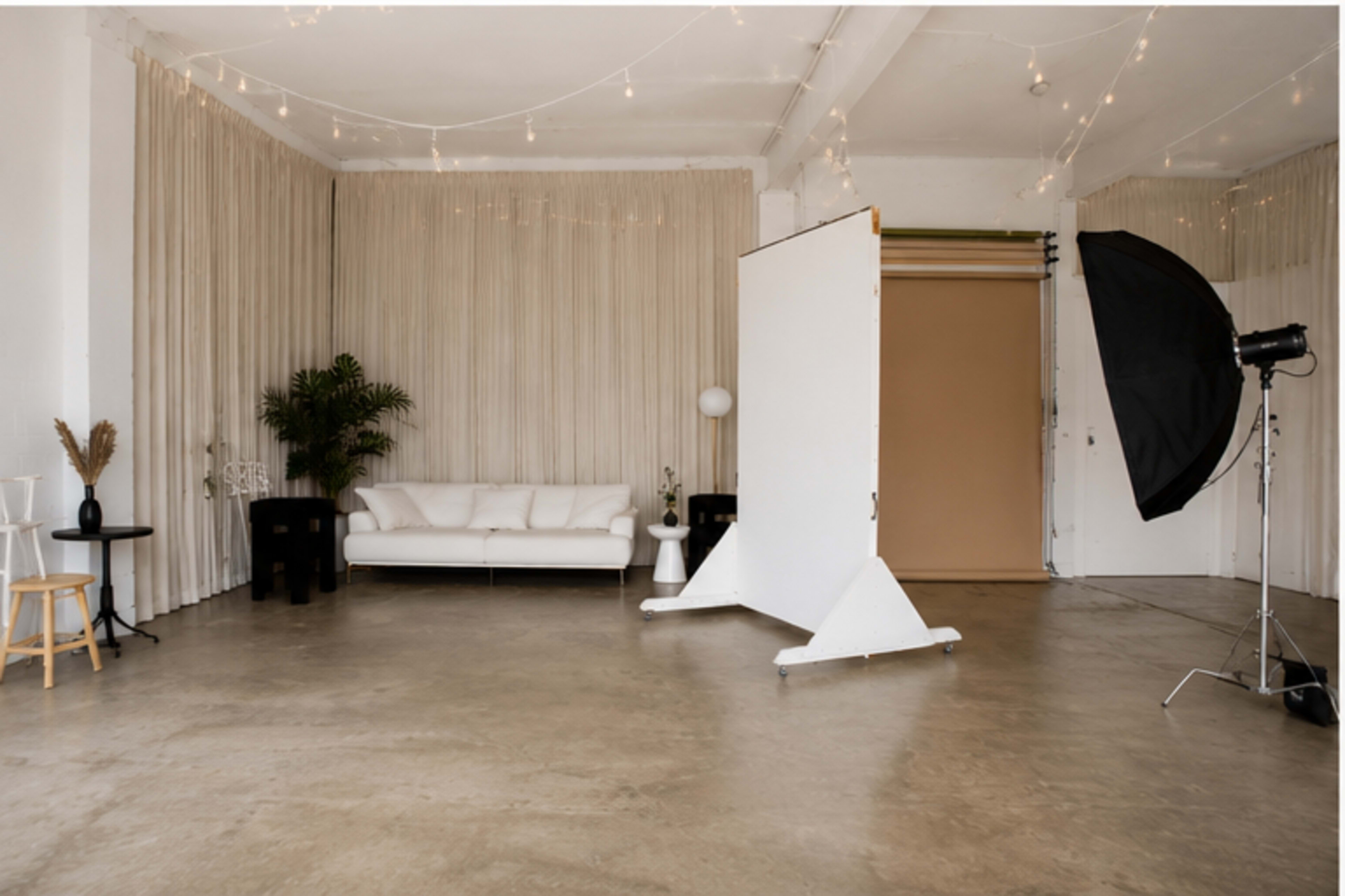 The image shows a spacious photography studio featuring a white sofa, background drapes, and lighting equipment.