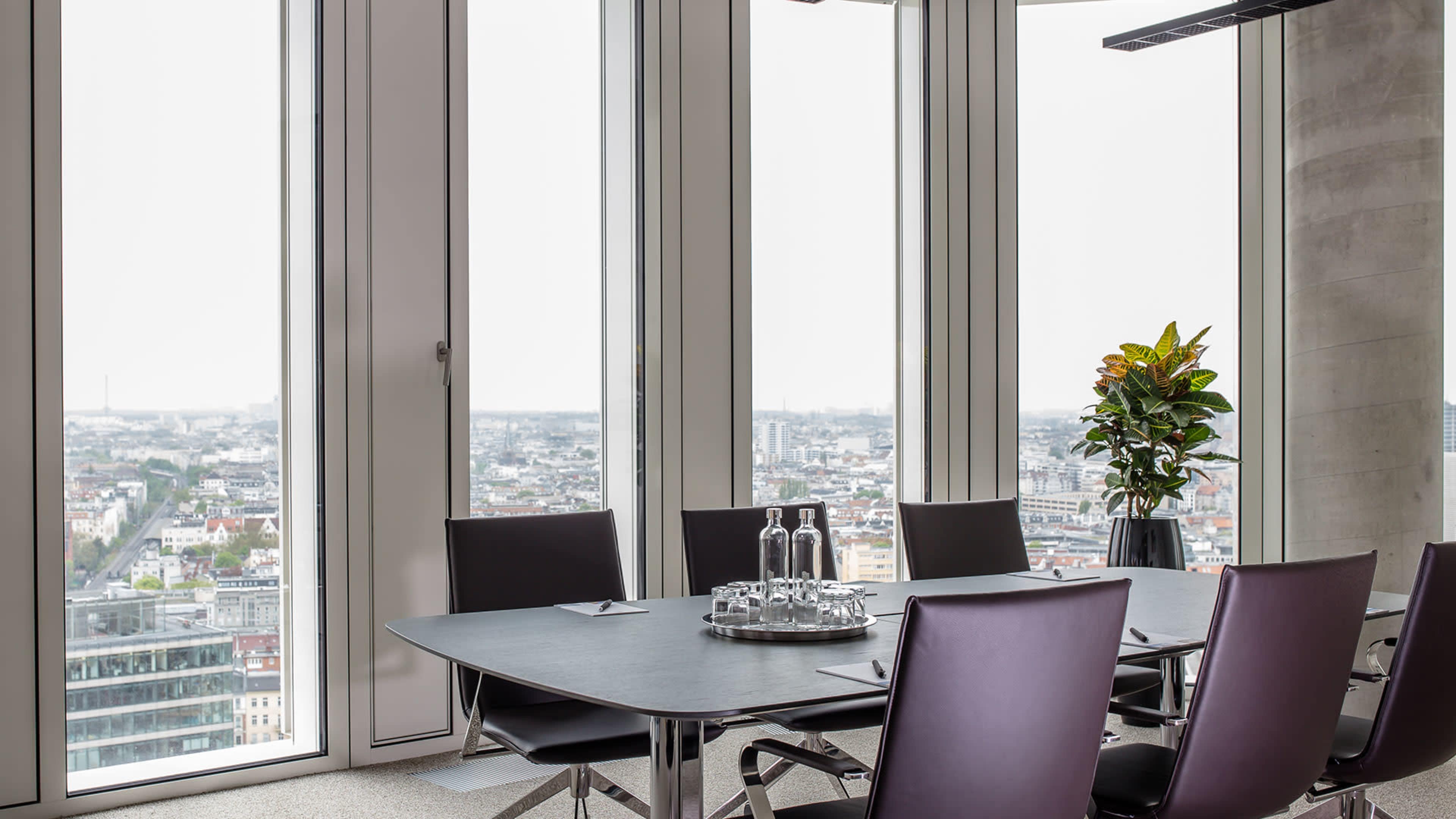 A modern conference room with a large table set for a meeting, featuring a view of a city skyline through large windows.