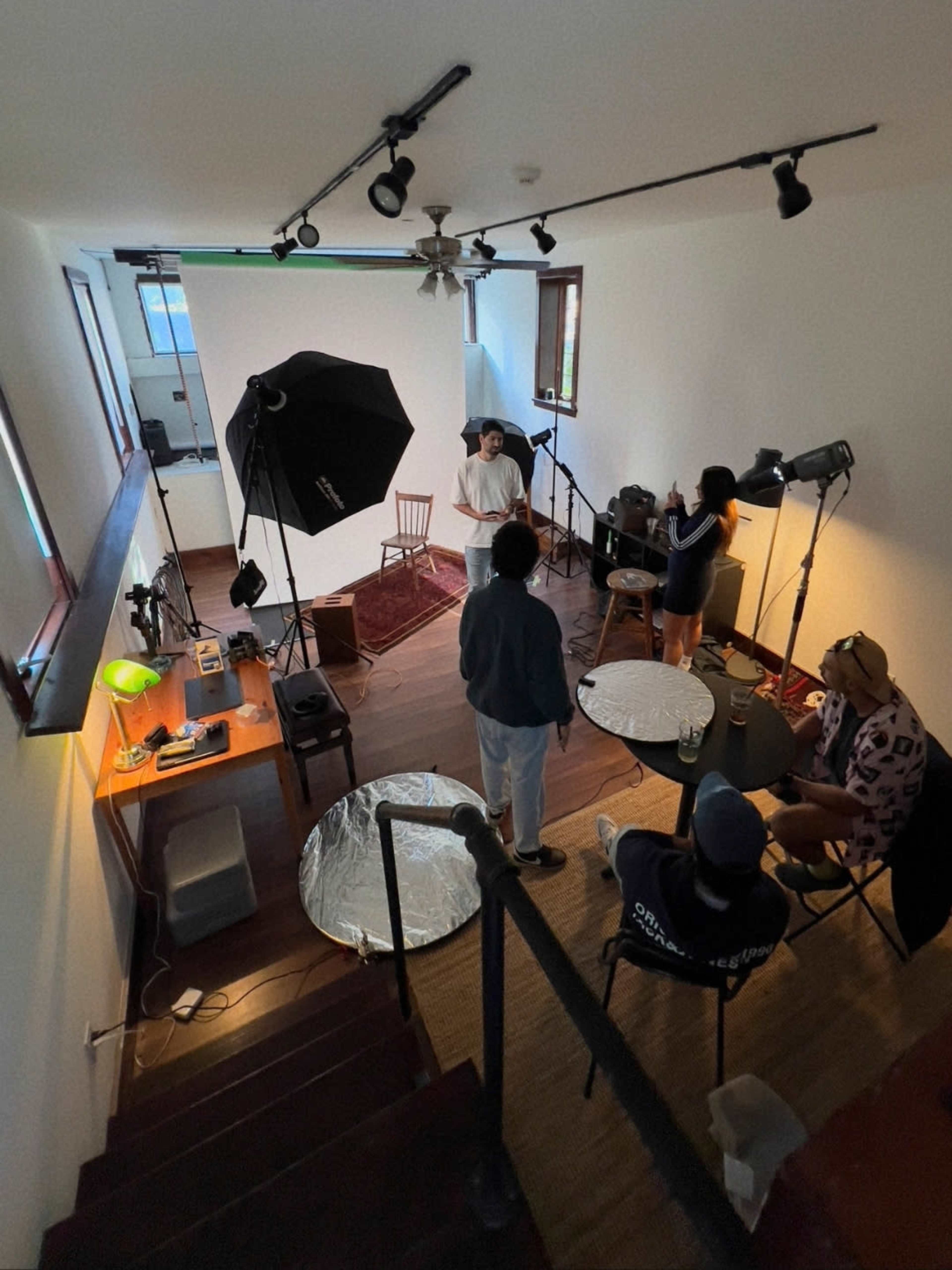 A small studio space with multiple lighting setups and equipment for a photoshoot or video recording, featuring a group of four people engaging in a session.