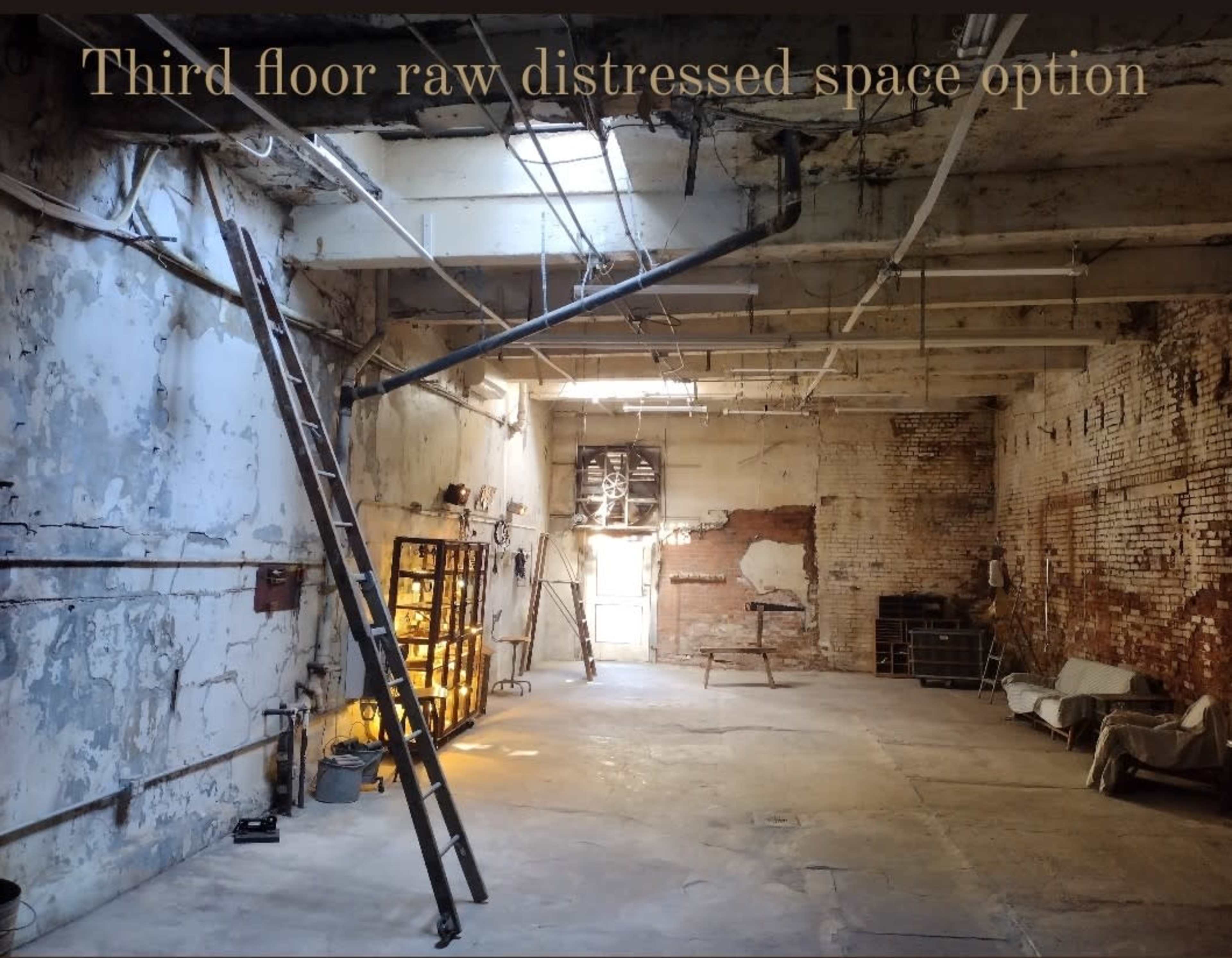 A spacious, unfinished room with exposed brick walls, large windows, and industrial elements like a metal ladder and shelving.