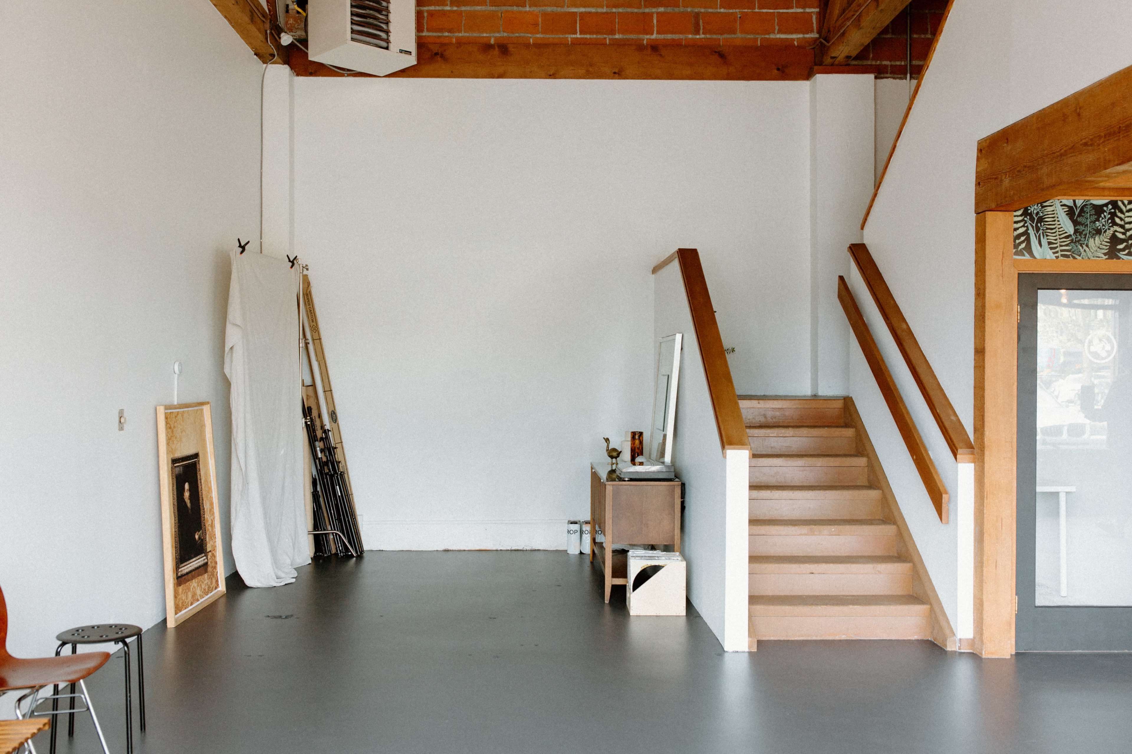An interior space with a staircase on the right, a small table with items, and some art supplies leaning against the wall.